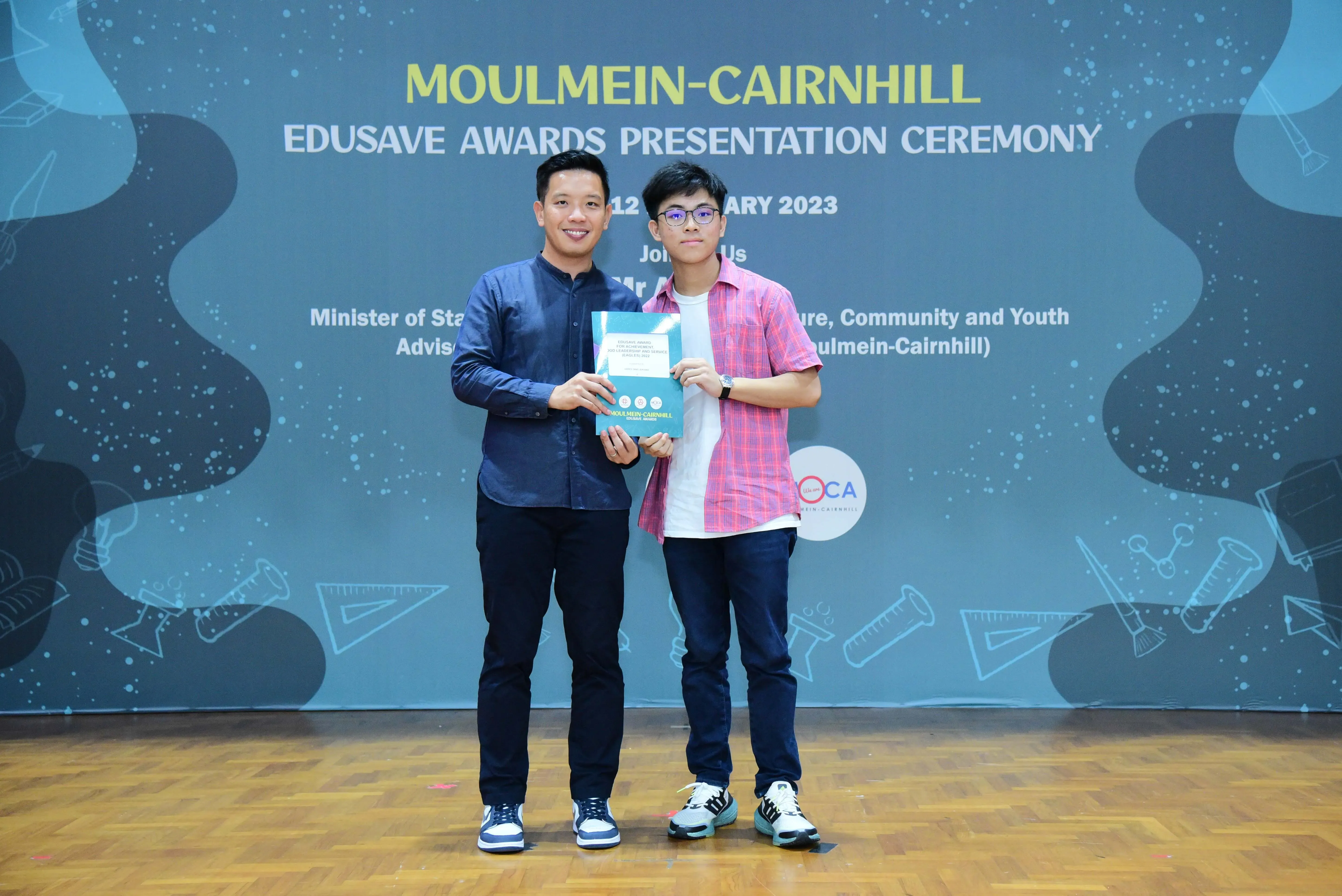 Two men hold an award booklet at the Moulmein-Cairnhill Edusave Awards Presentation Ceremony 2023.