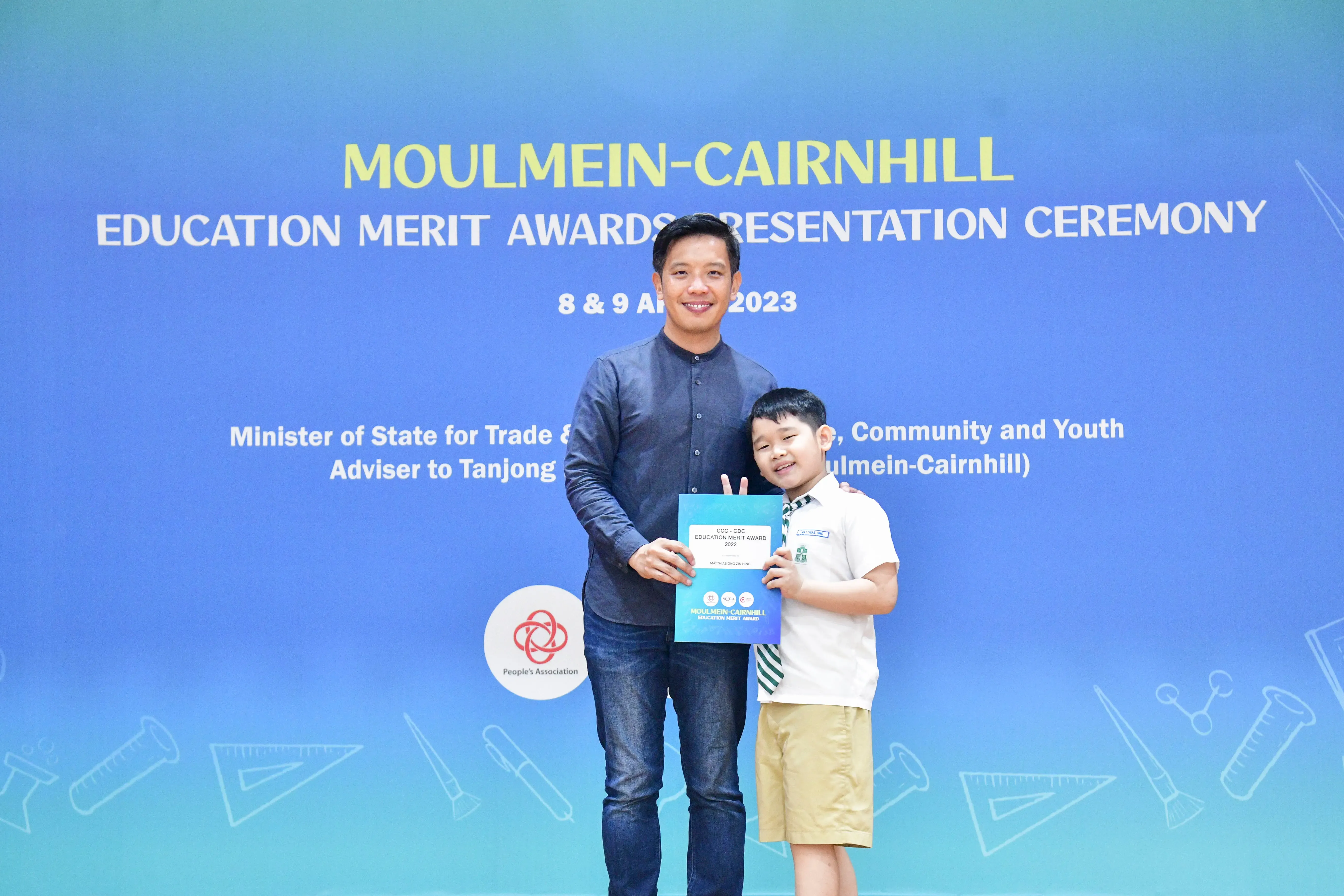 An adult and a young boy hold an award certificate at the Moulmein-Cairnhill Education Merit Awards Ceremony 2023.