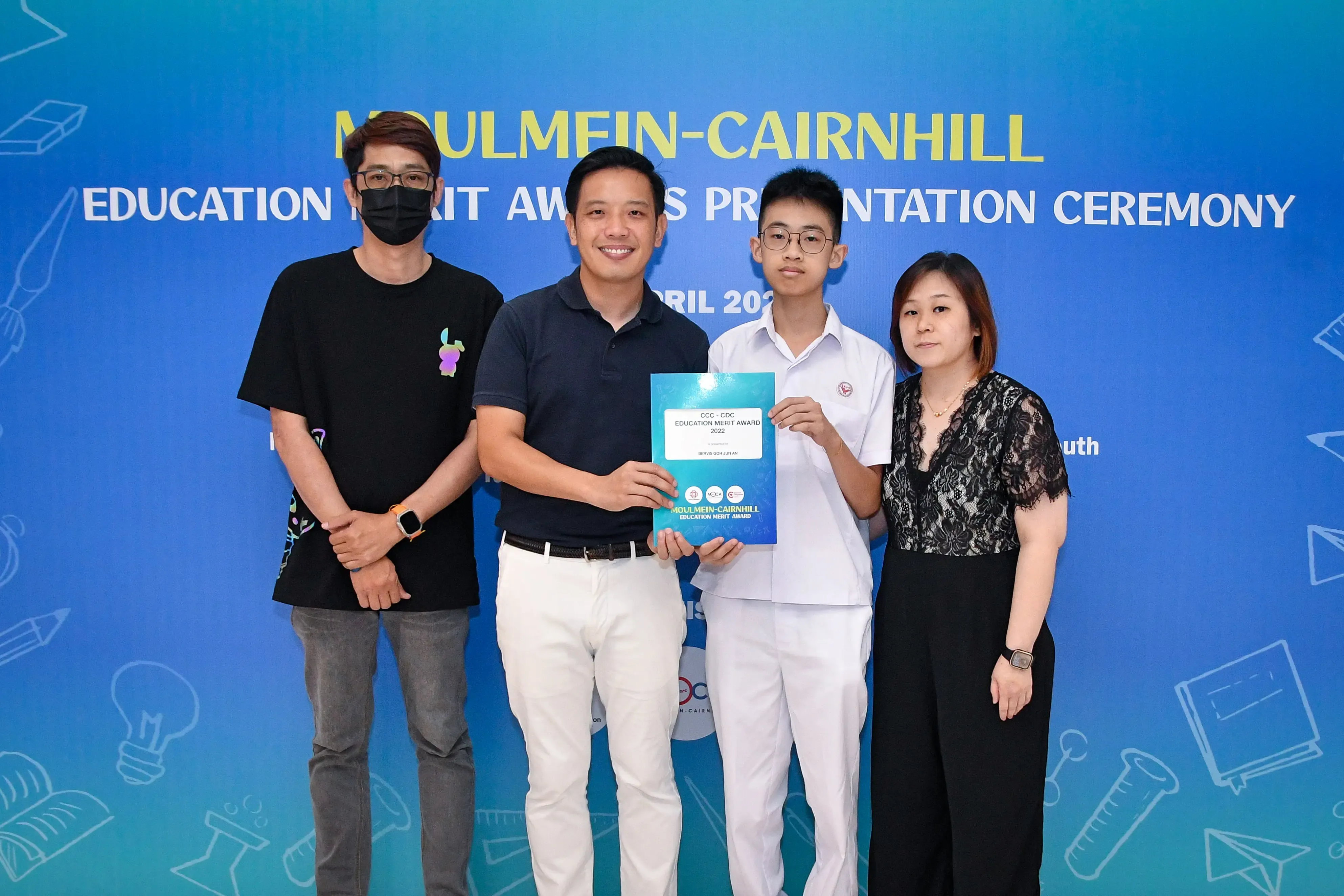 Four people pose at the Moulmein-Cairnhill Education Merit Awards Presentation Ceremony, two holding a blue award certificate.