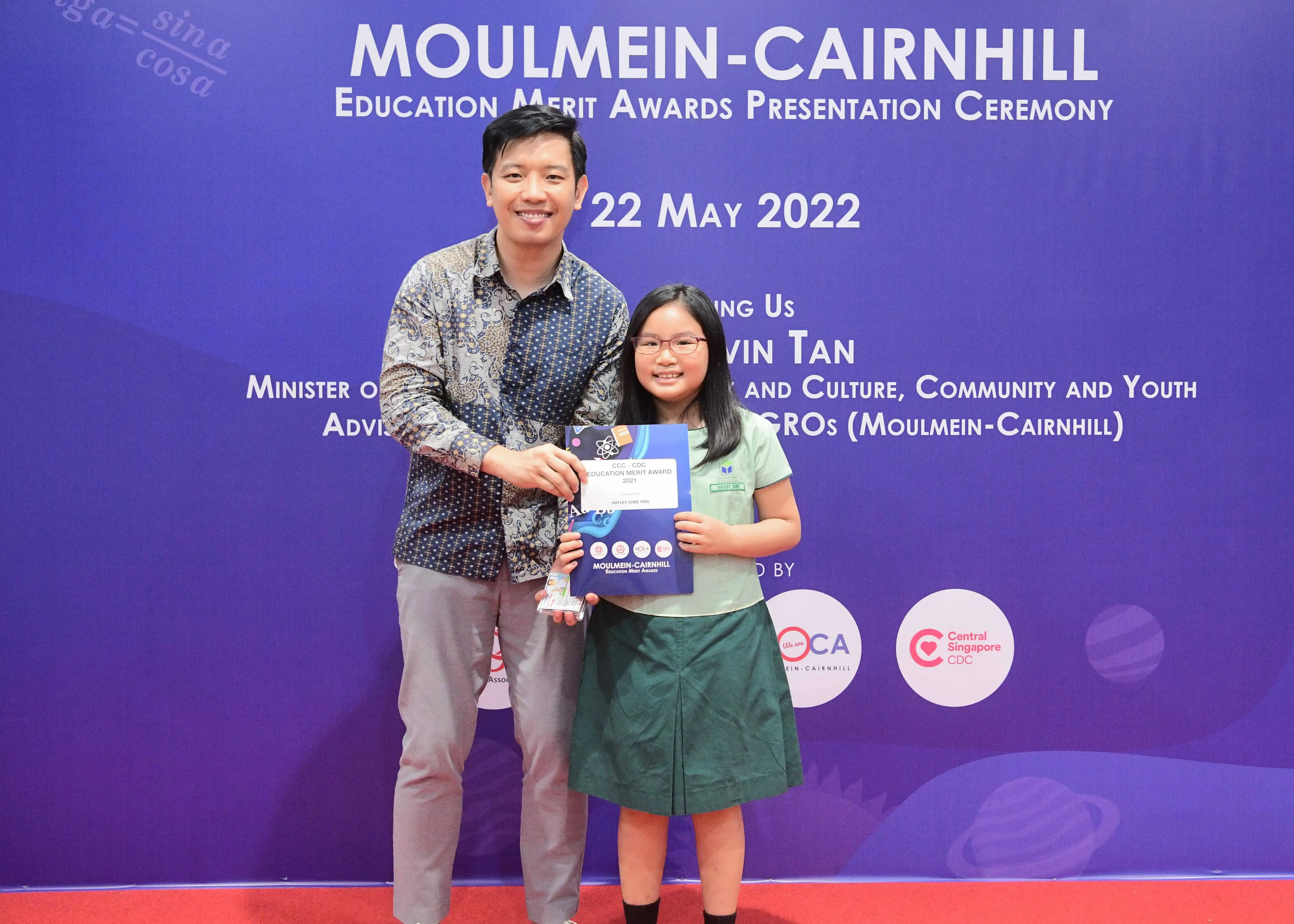 A man and a young girl pose together holding an award certificate at the Moulmein-Cairnhill Education Merit Awards ceremony.
