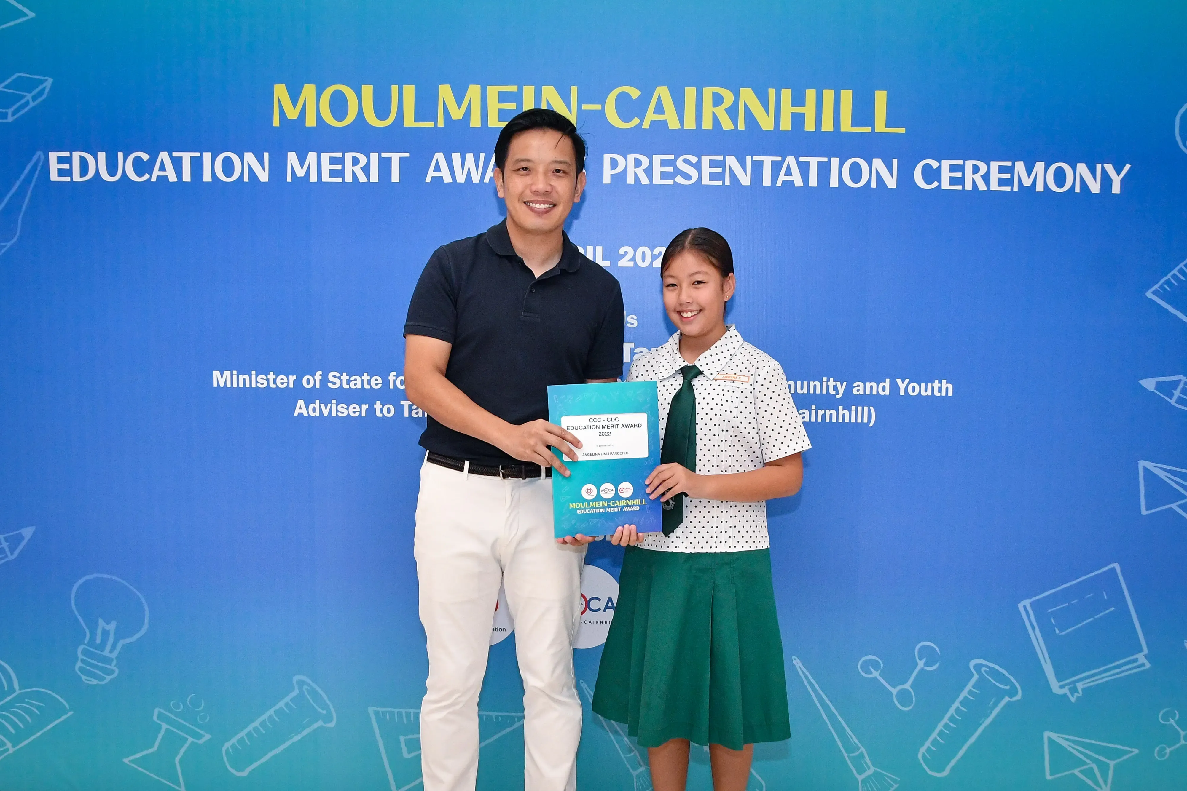 A man and a young girl in school uniform hold an award certificate at the Moulmein-Cairnhill Education Merit Award ceremony.
