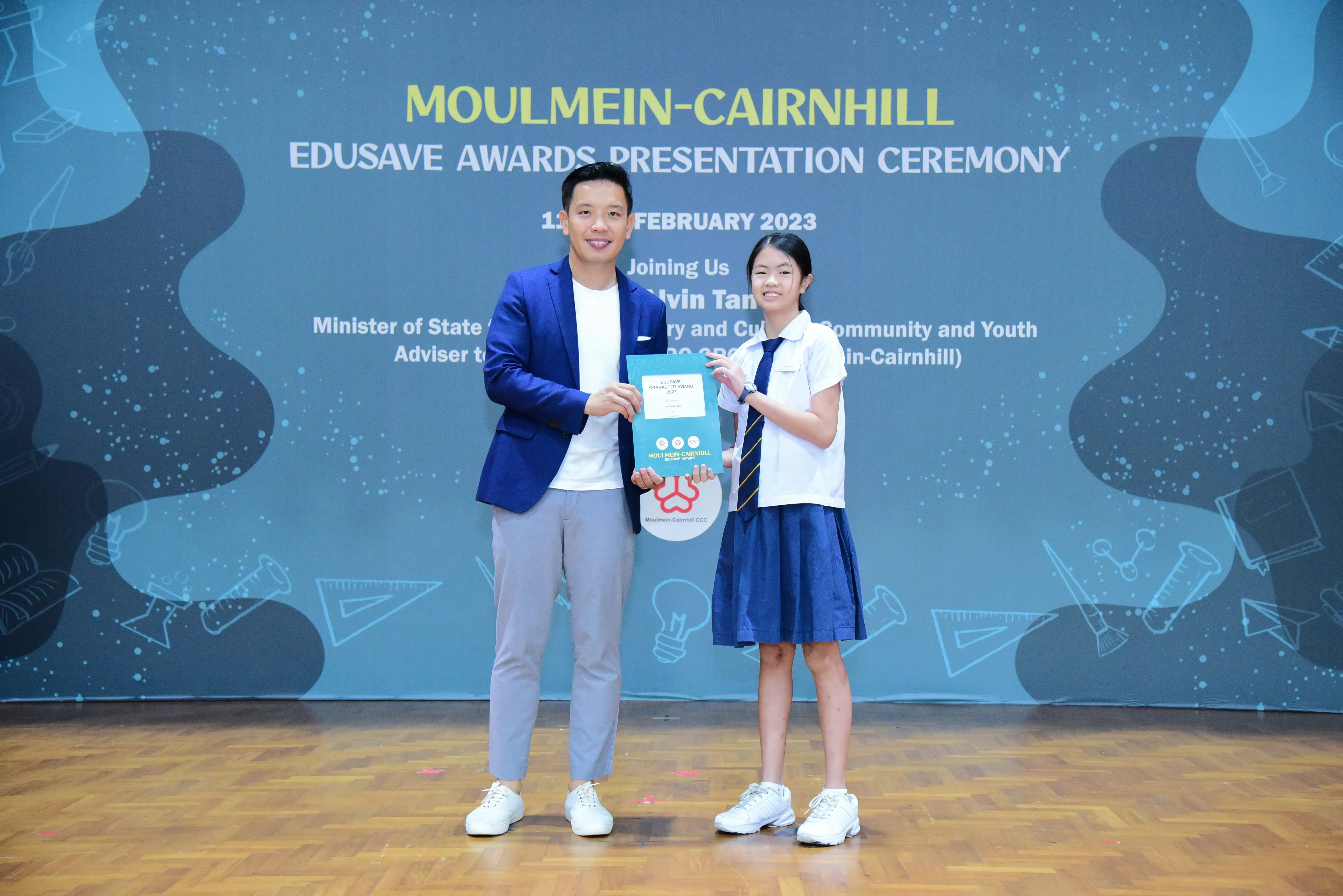A man in a blue blazer and a girl in school uniform hold an award at the Moulmein-Cairnhill Edusave Awards Ceremony 2023.