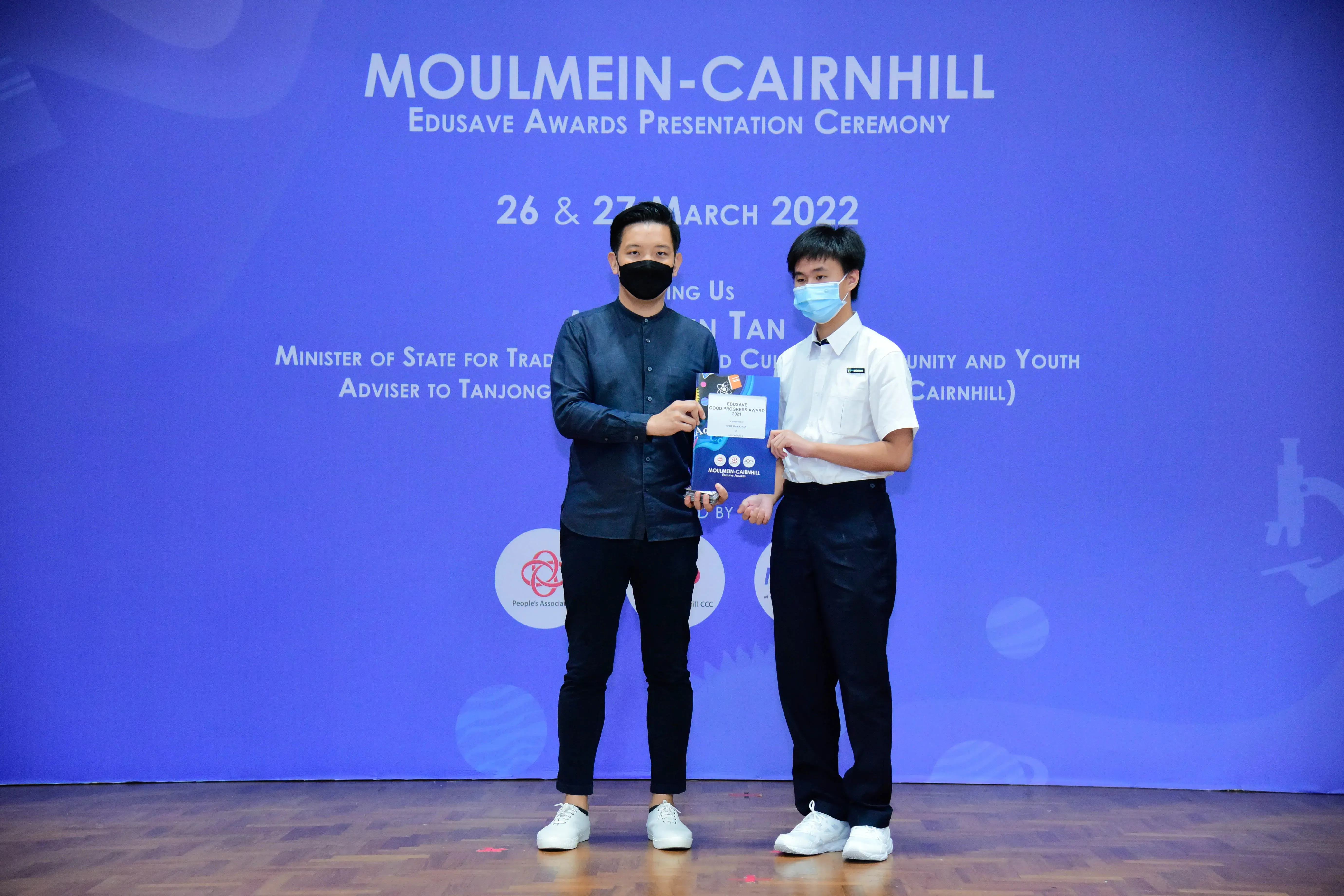 Two masked men hold a certificate at the Moulmein-Cairnhill Edusave Awards Presentation Ceremony, March 2022.