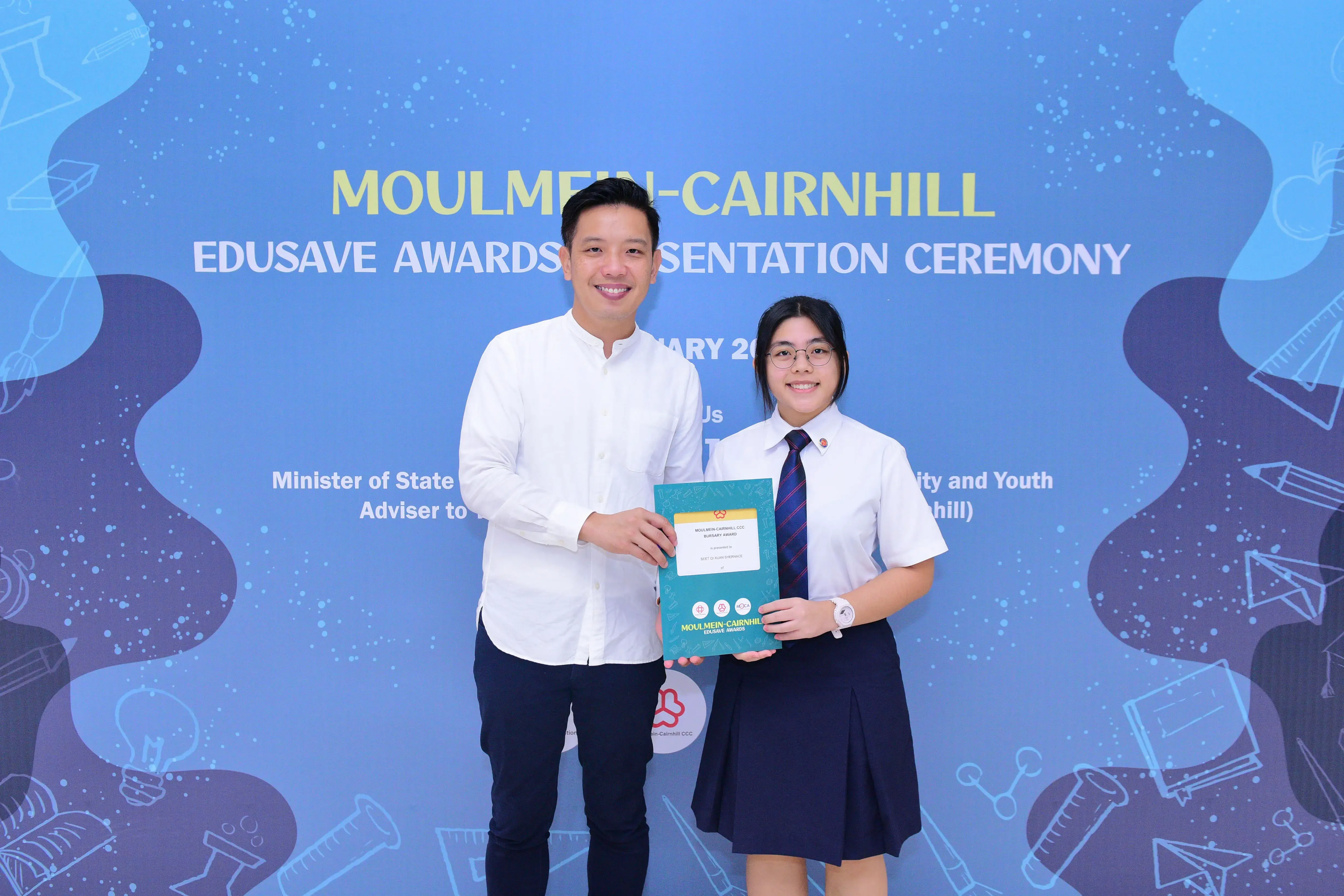Two people smile holding a certificate at the Moulmein-Cairnhill Edusave Awards Presentation Ceremony backdrop.