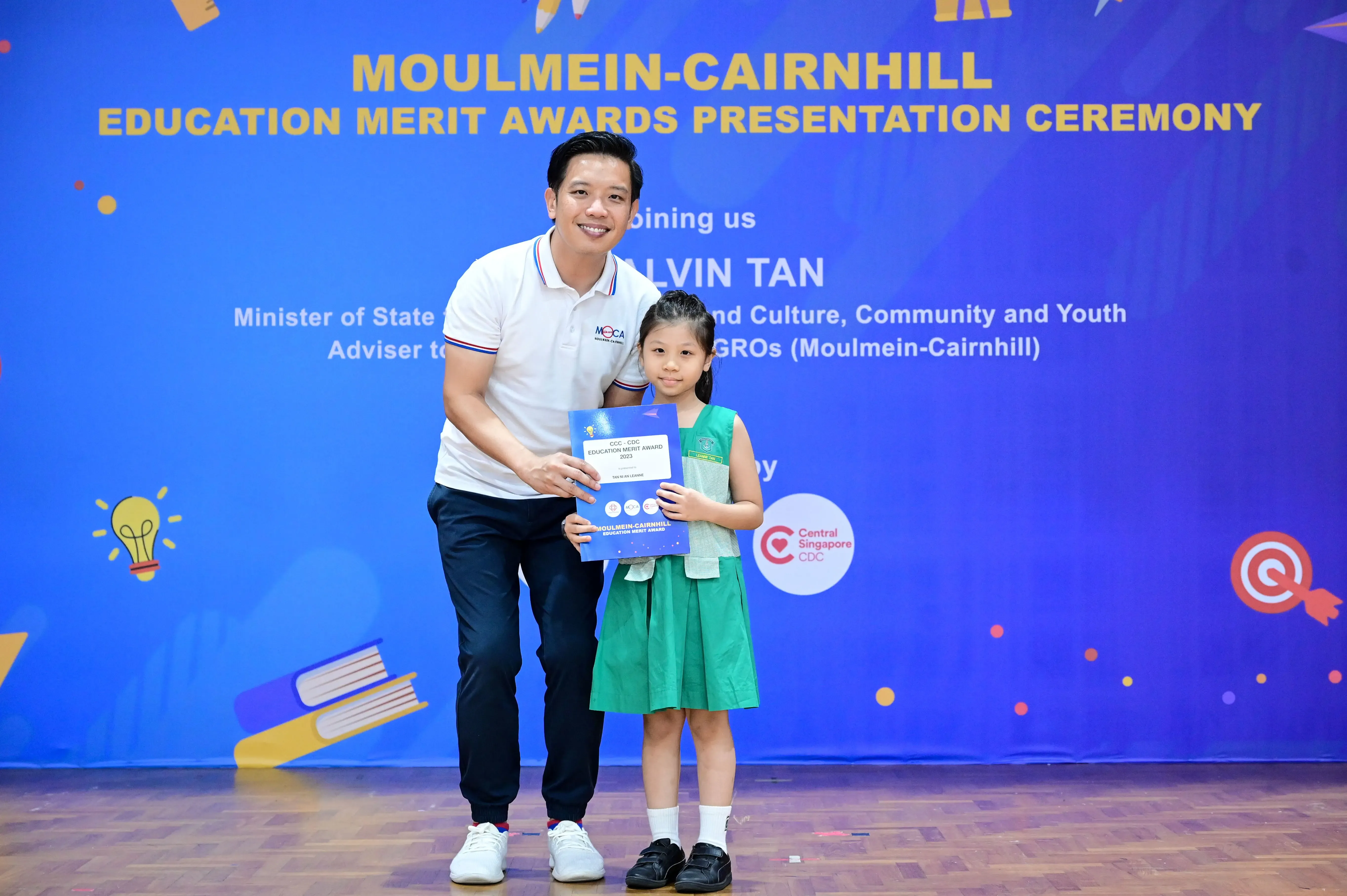 A man and a young girl hold a certificate at the Moulmein-Cairnhill Education Merit Awards Presentation Ceremony.