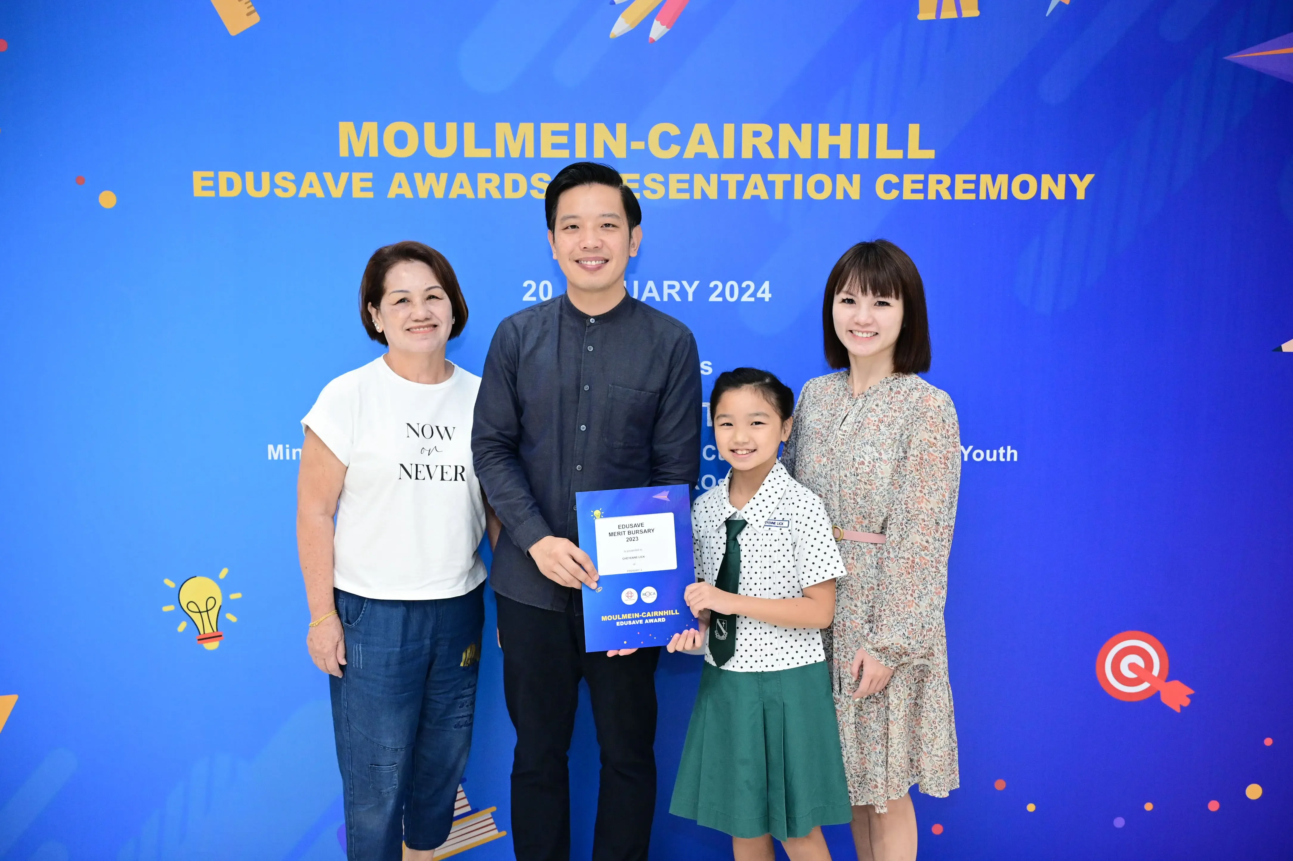 Four people pose at the Moulmein-Cairnhill Edusave Awards Presentation Ceremony, holding a merit bursary certificate.