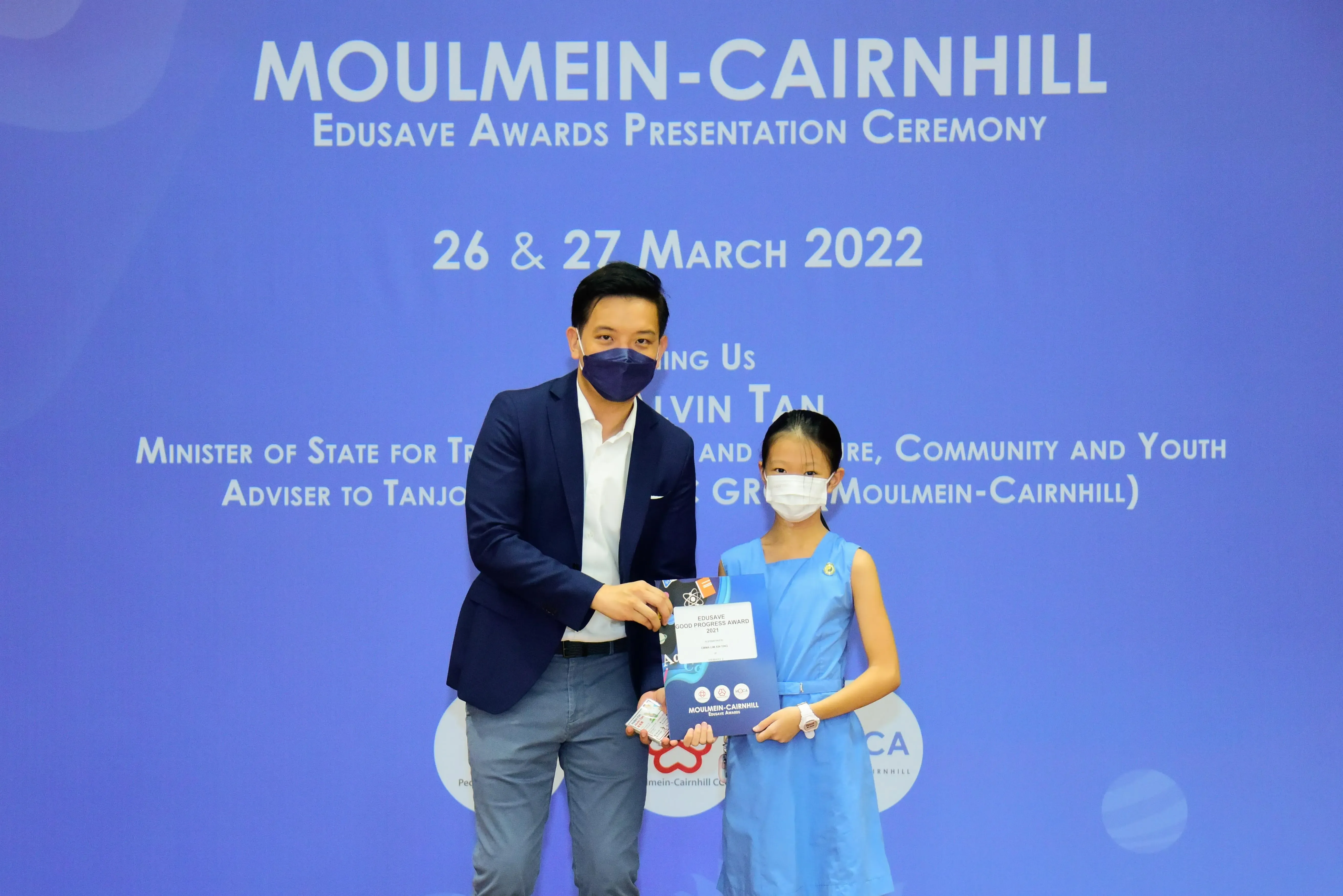 A man and a young girl in masks hold an award certificate at the Moulmein-Cairnhill Edusave Awards Ceremony, March 2022.