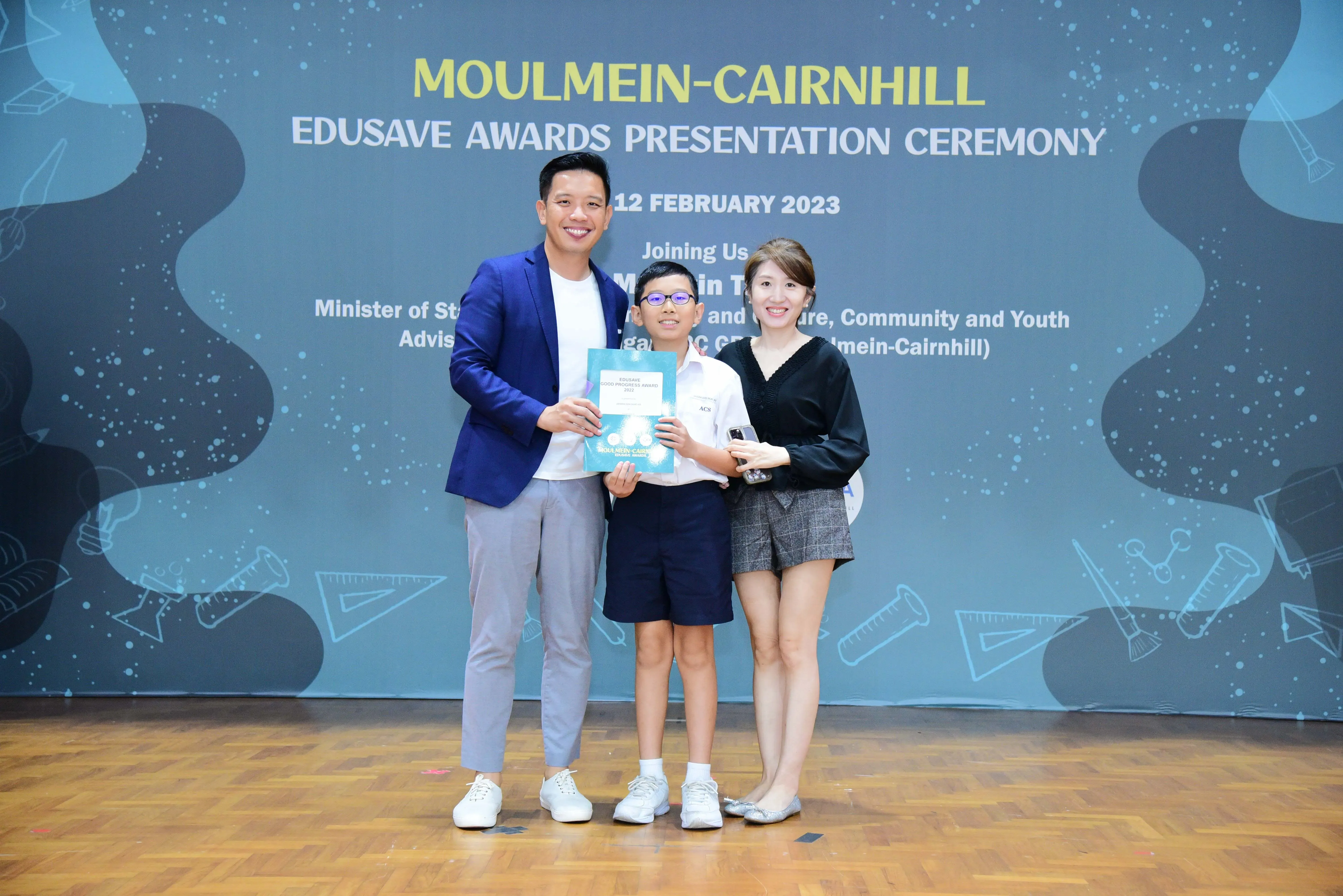 Two adults and a young boy pose with an award at the Moulmein-Cairnhill Edusave Awards Presentation Ceremony, February 2023.