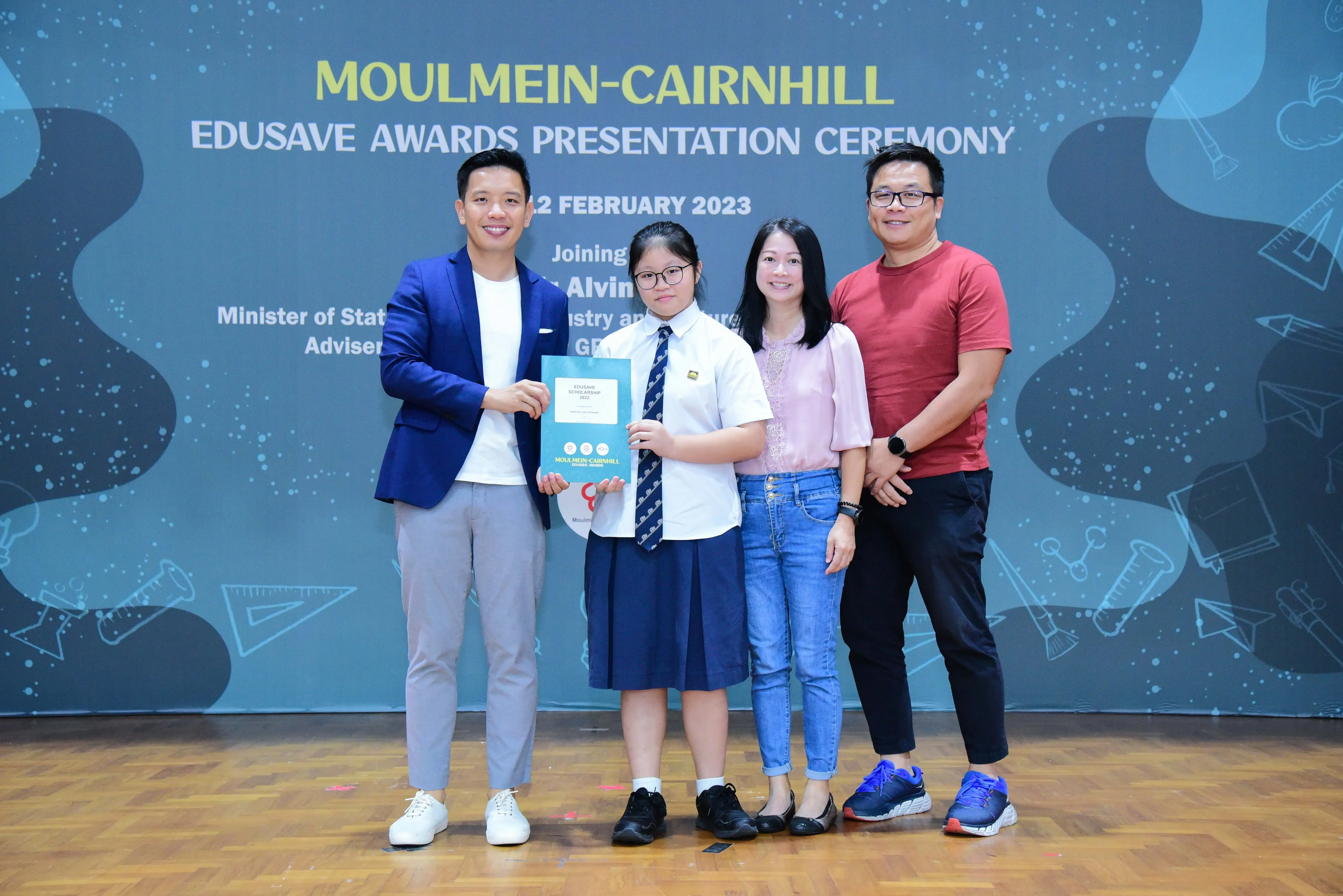 Four people pose at the Moulmein-Cairnhill Edusave Awards Presentation Ceremony, with a student holding a certificate.