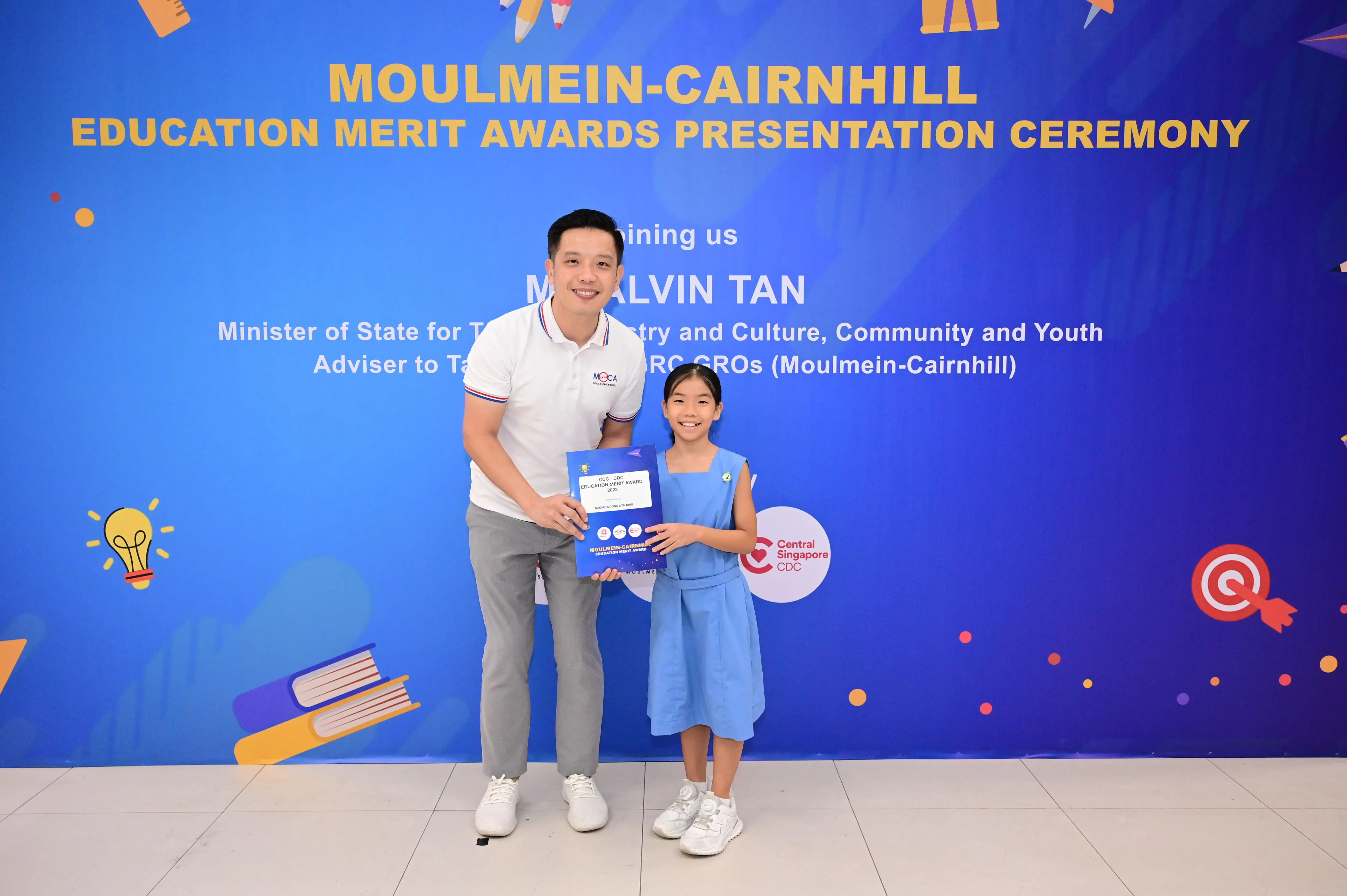 A man and a young girl hold an award certificate at the Moulmein-Cairnhill Education Merit Awards Presentation Ceremony.