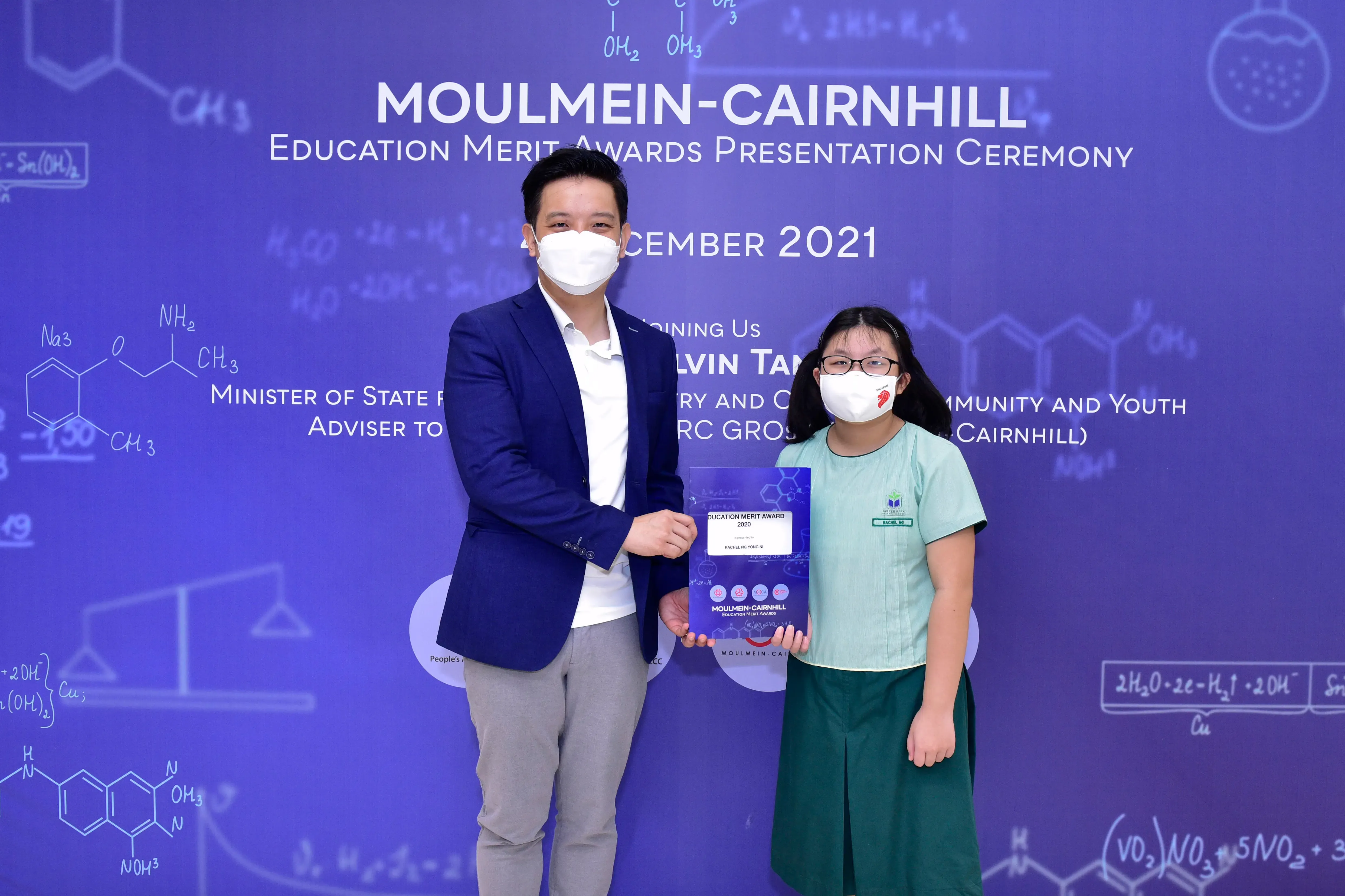 Two masked individuals hold an award plaque at the Moulmein-Cairnhill Education Merit Awards Ceremony, December 2021.