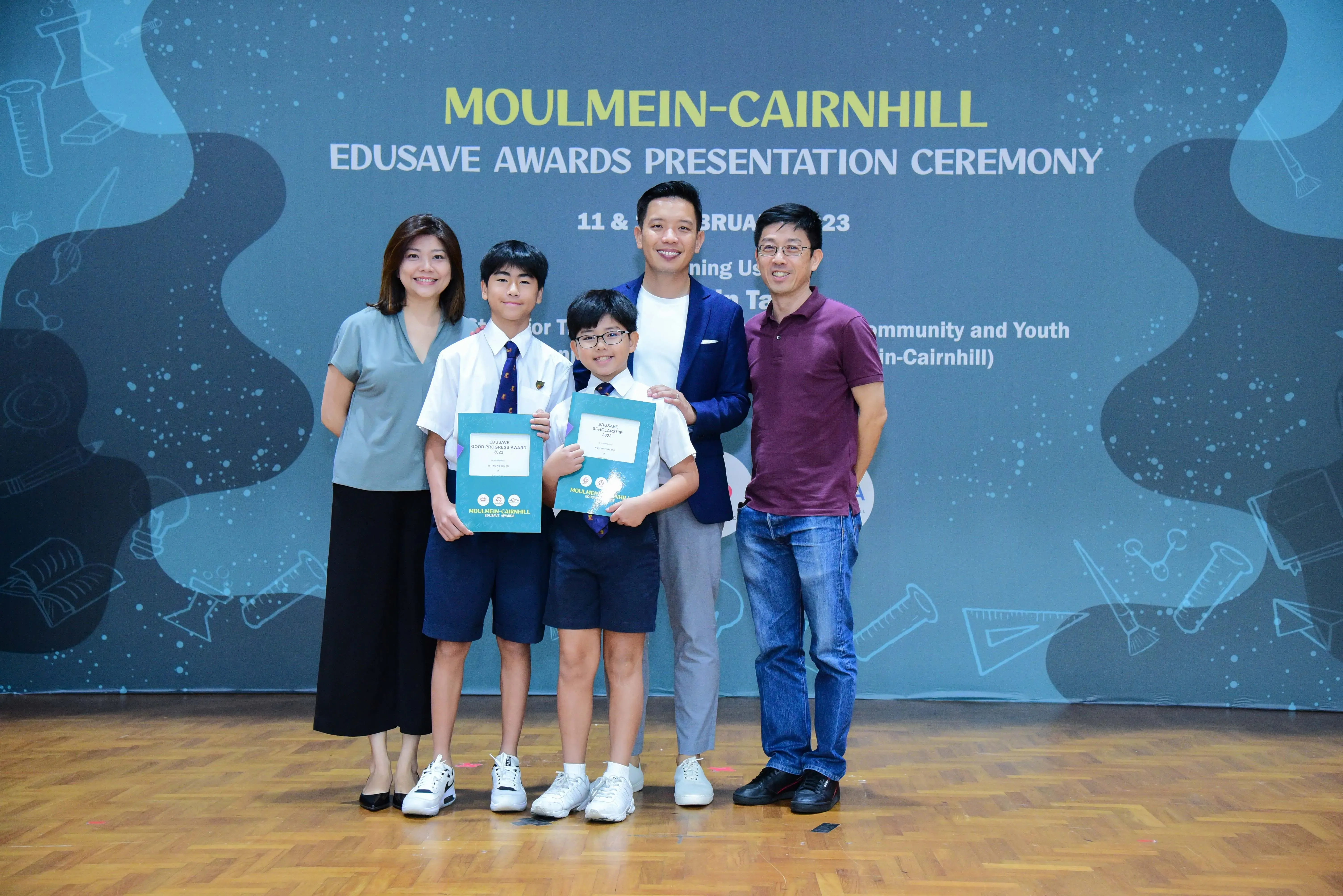 Five people pose at the Moulmein-Cairnhill Edusave Awards Presentation Ceremony, two boys holding award certificates.