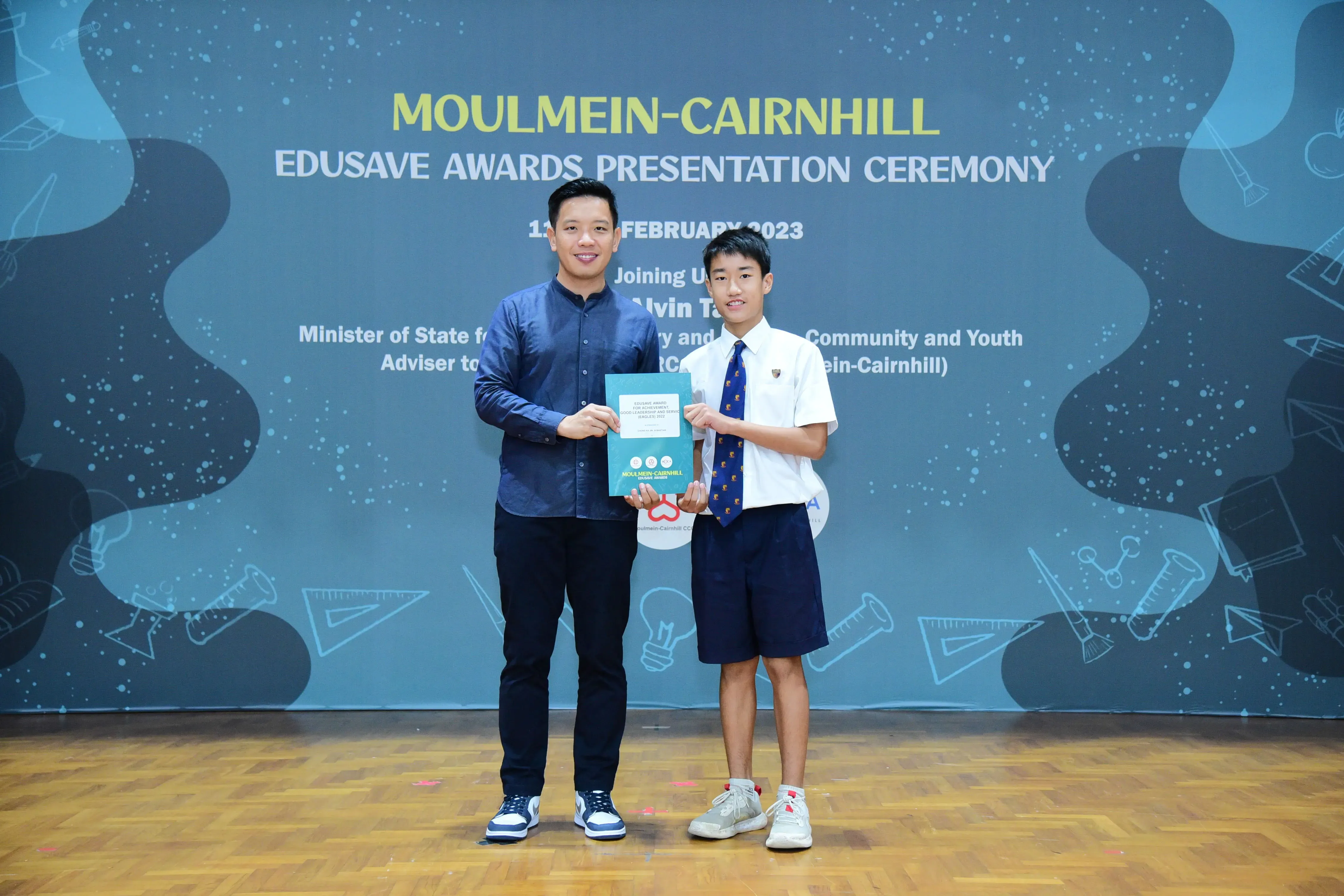 Two people hold a certificate together at the Moulmein-Cairnhill Edusave Awards Presentation Ceremony in February 2023.