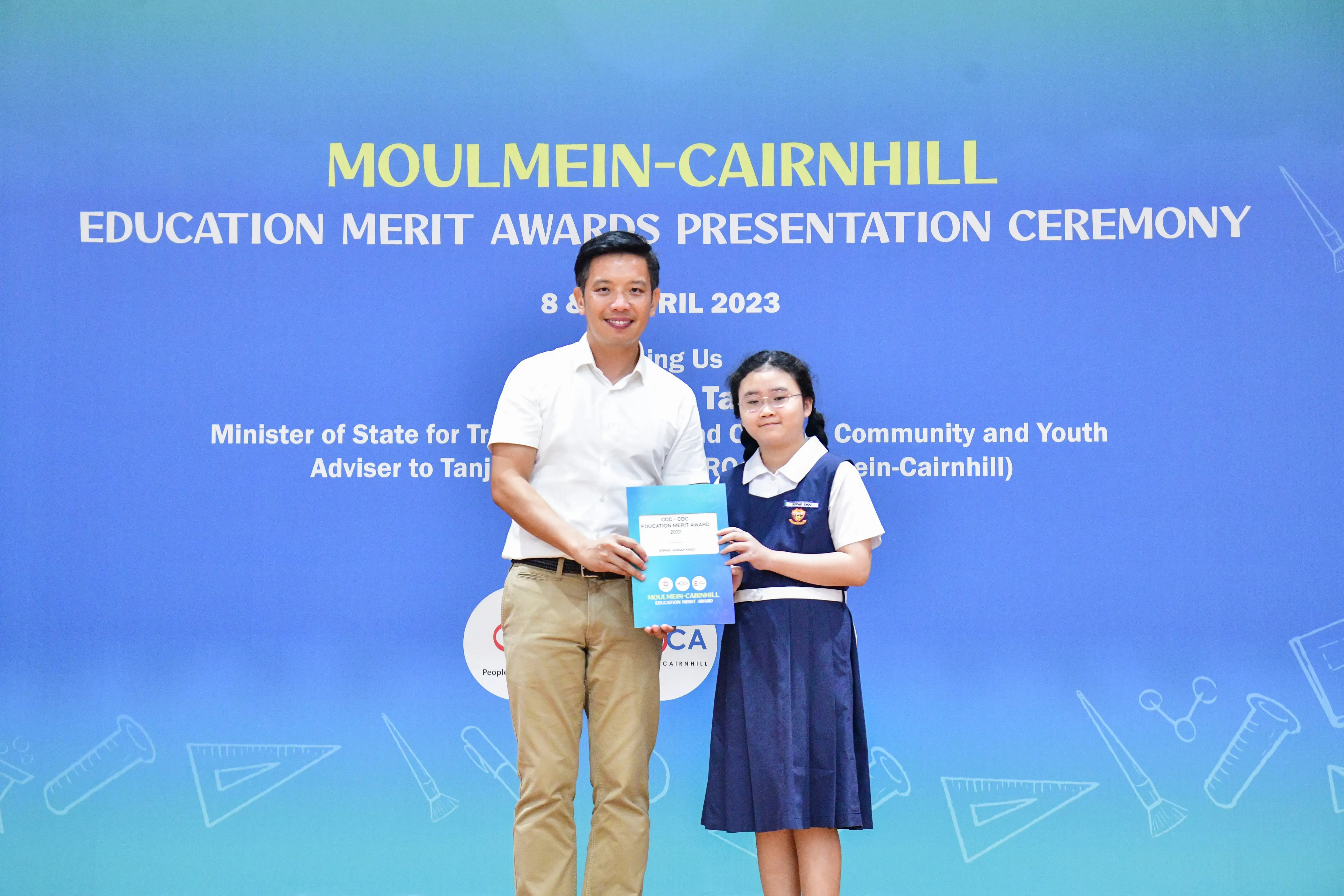 A man and a young girl hold an award certificate at the Moulmein-Cairnhill Education Merit Awards Ceremony 2023.