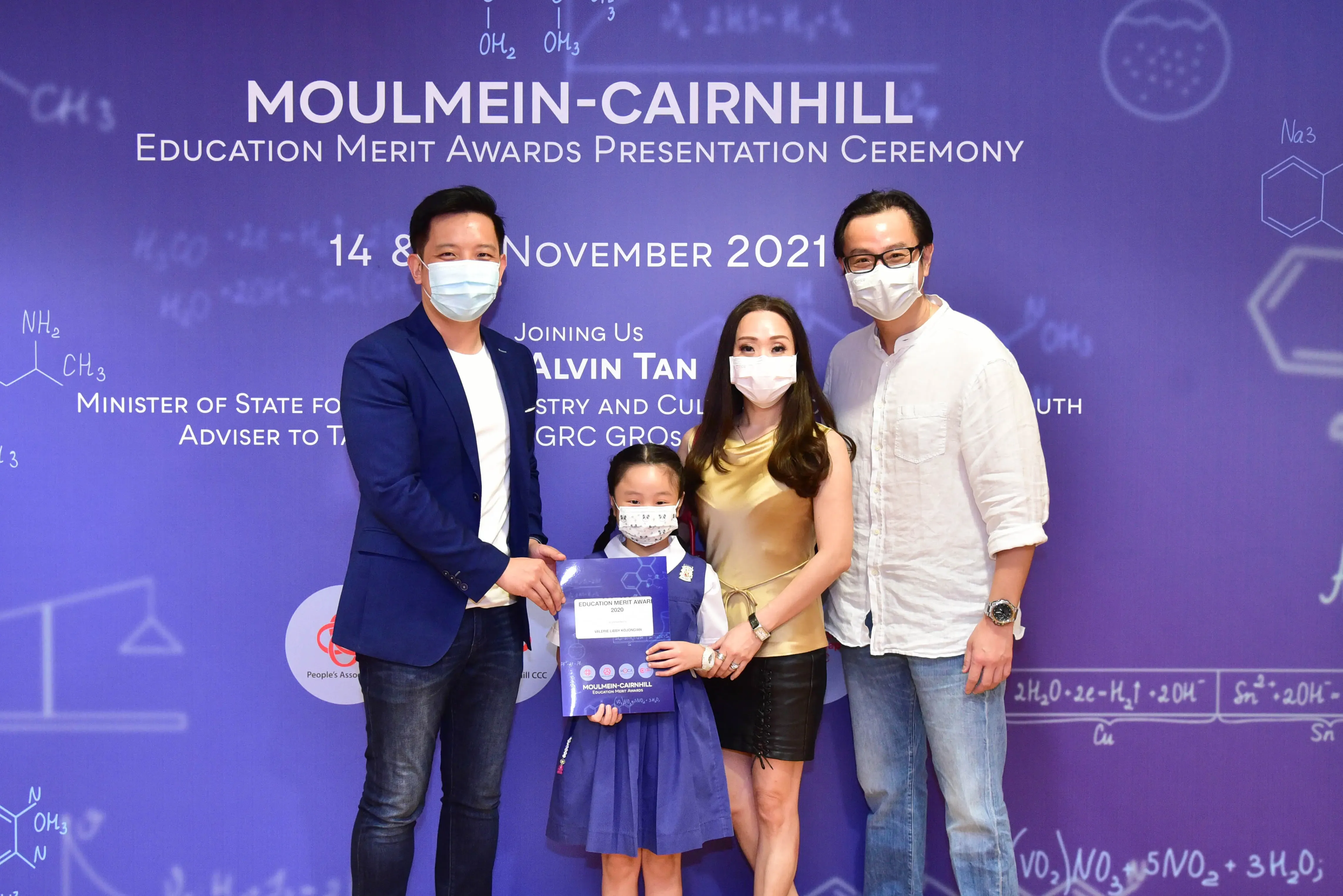 Four masked people, including a young girl holding a certificate, pose at the Moulmein-Cairnhill Education Merit Awards 2021.