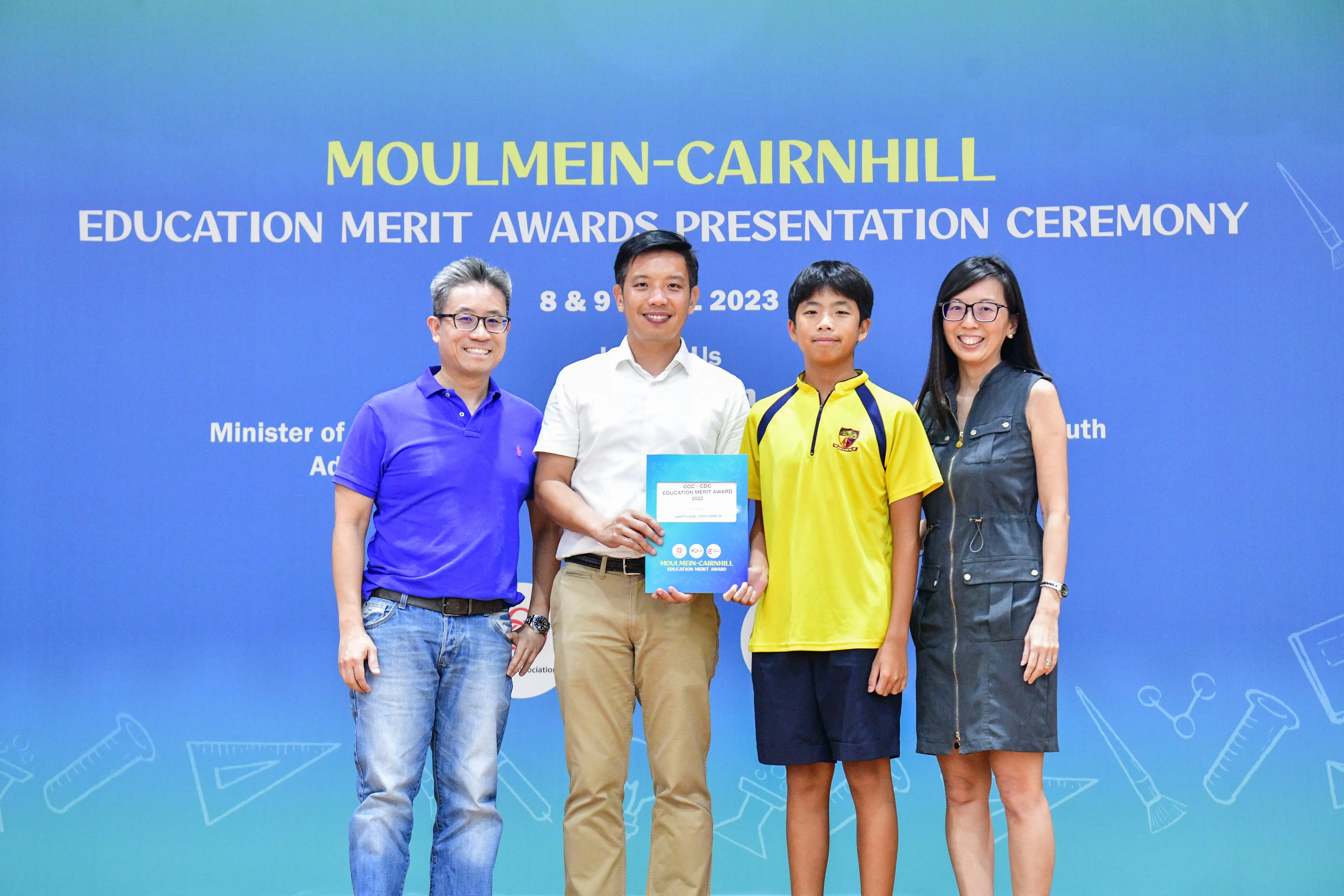 Four people pose at the Moulmein-Cairnhill Education Merit Awards Presentation Ceremony, with a student holding a certificate.