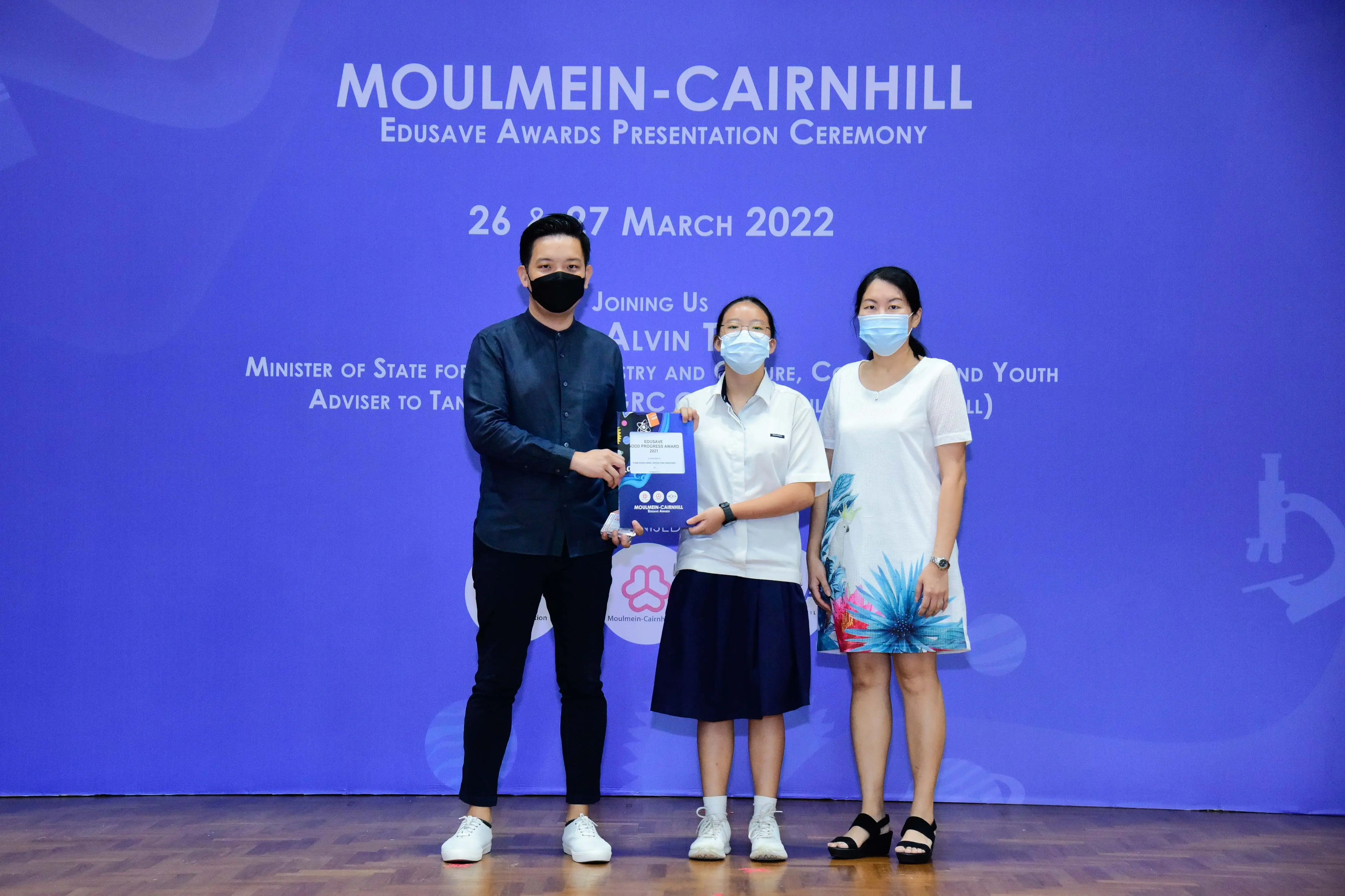 Three masked people pose on stage at the Moulmein-Cairnhill Edusave Awards Presentation Ceremony, March 2022.