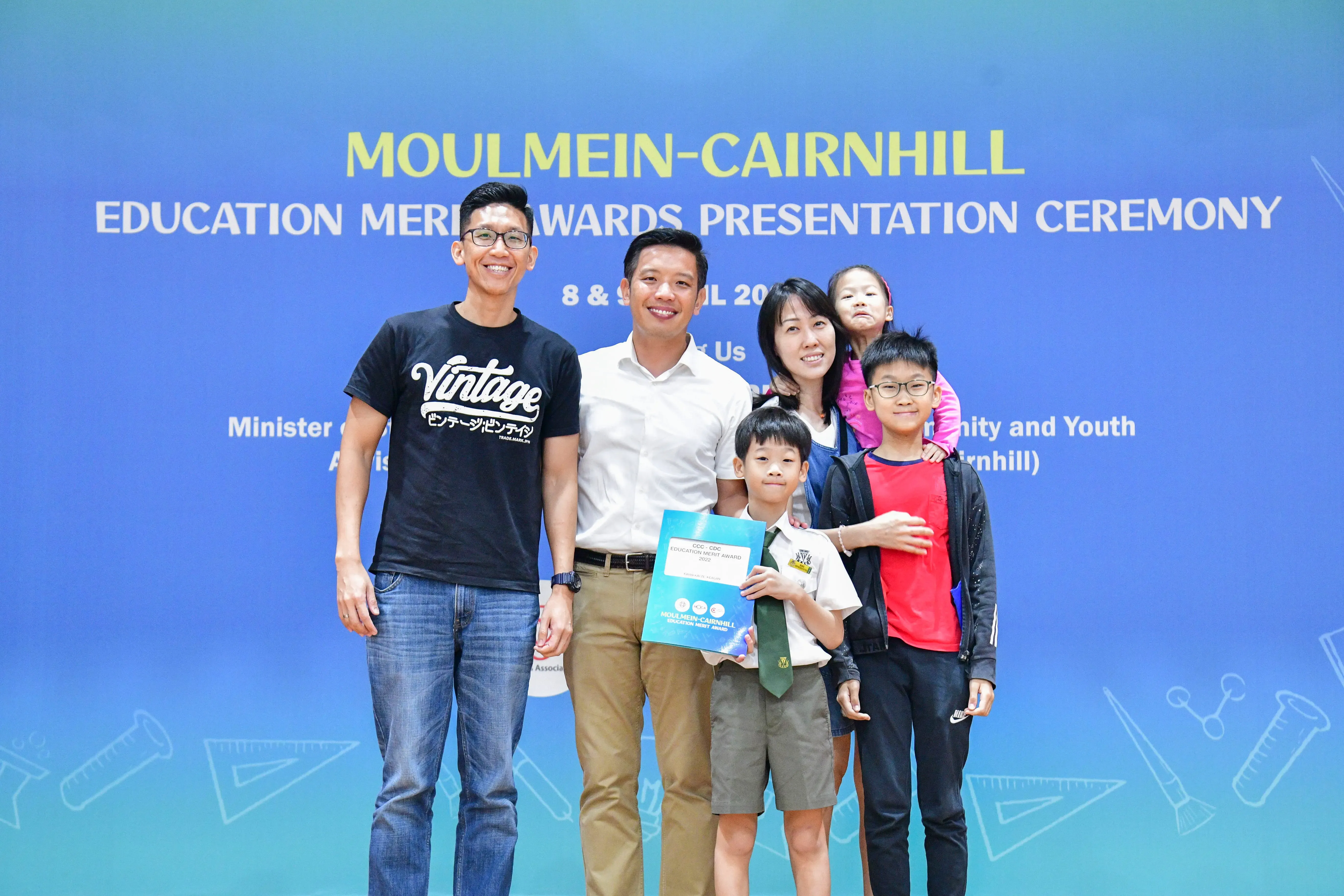 Family of five posing at the Moulmein-Cairnhill Education Merit Awards Presentation Ceremony, child holding an award folder.
