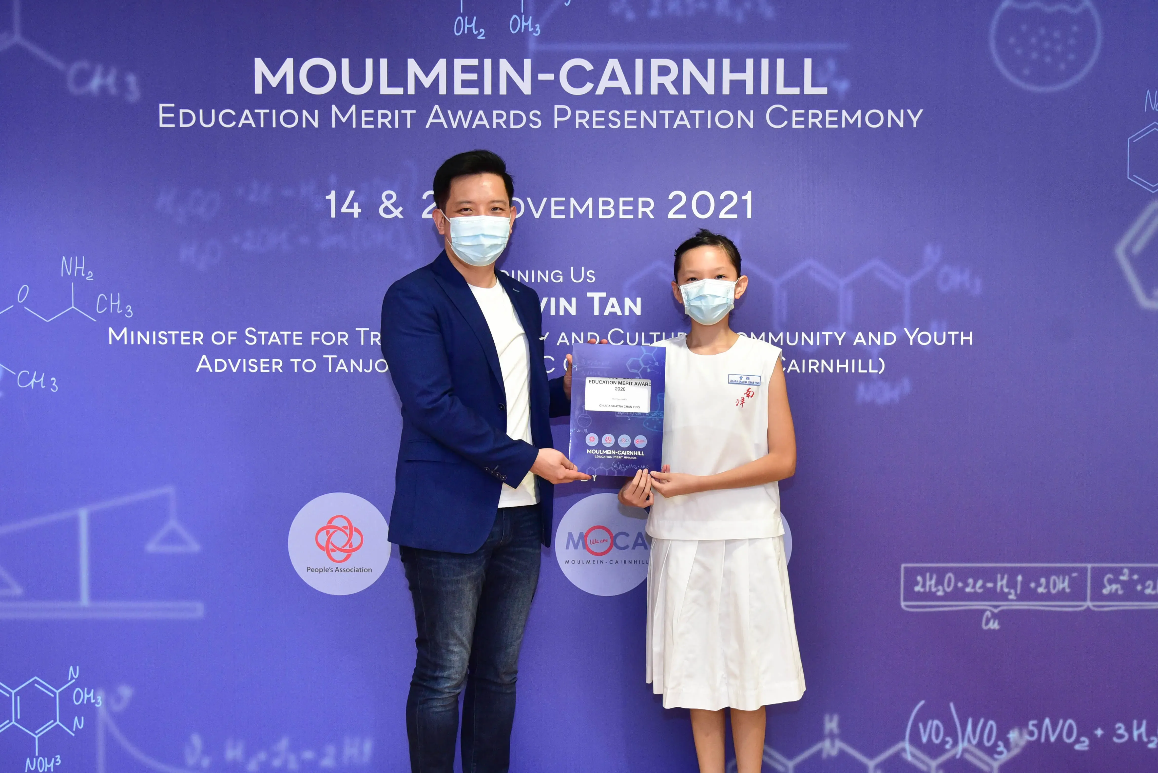 A man and a young girl in masks hold an award certificate at the Moulmein-Cairnhill Education Merit Awards 2021.