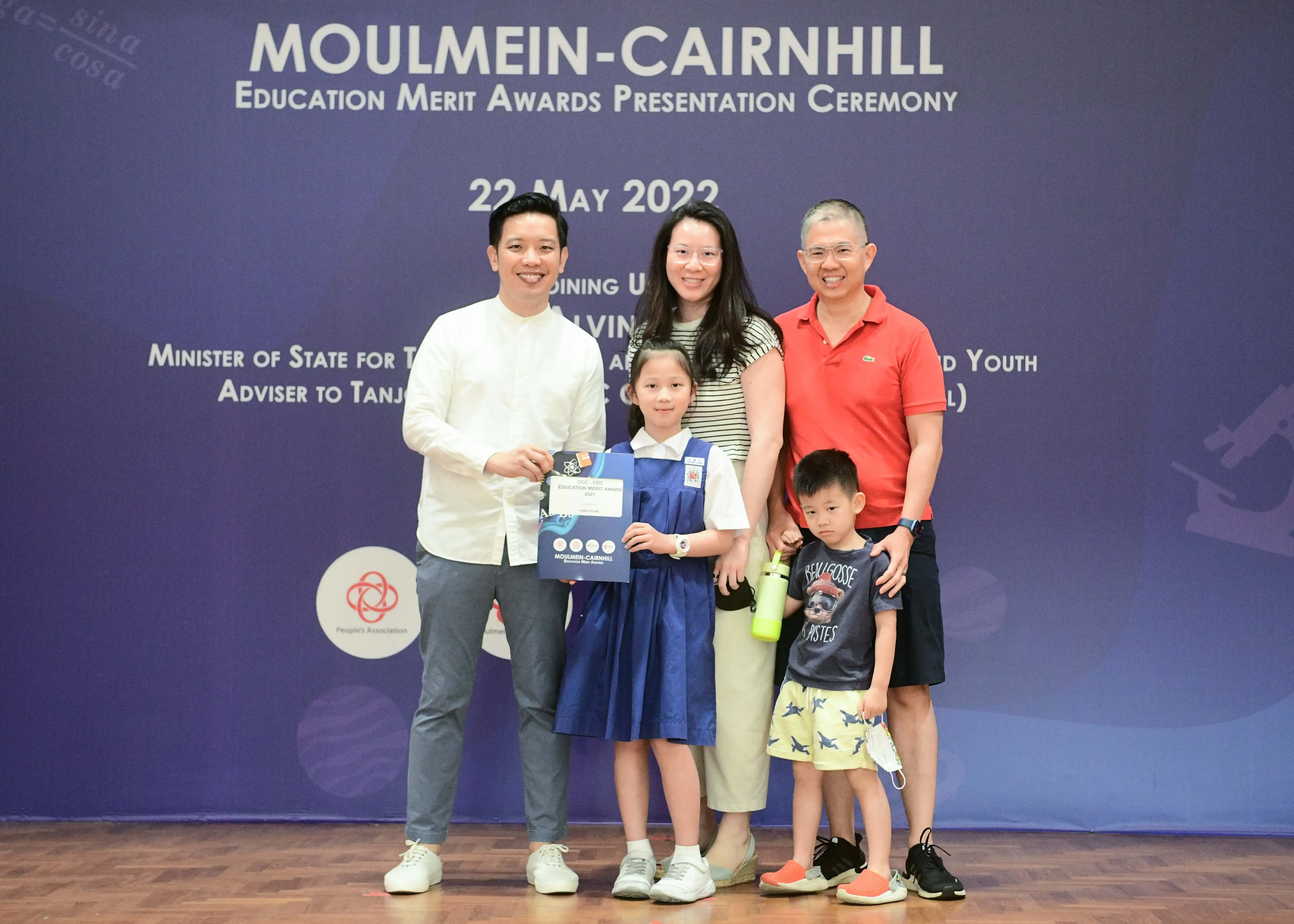 Five people pose at the Moulmein-Cairnhill Education Merit Awards Ceremony on 22 May 2022, with a girl holding an award certificate.
