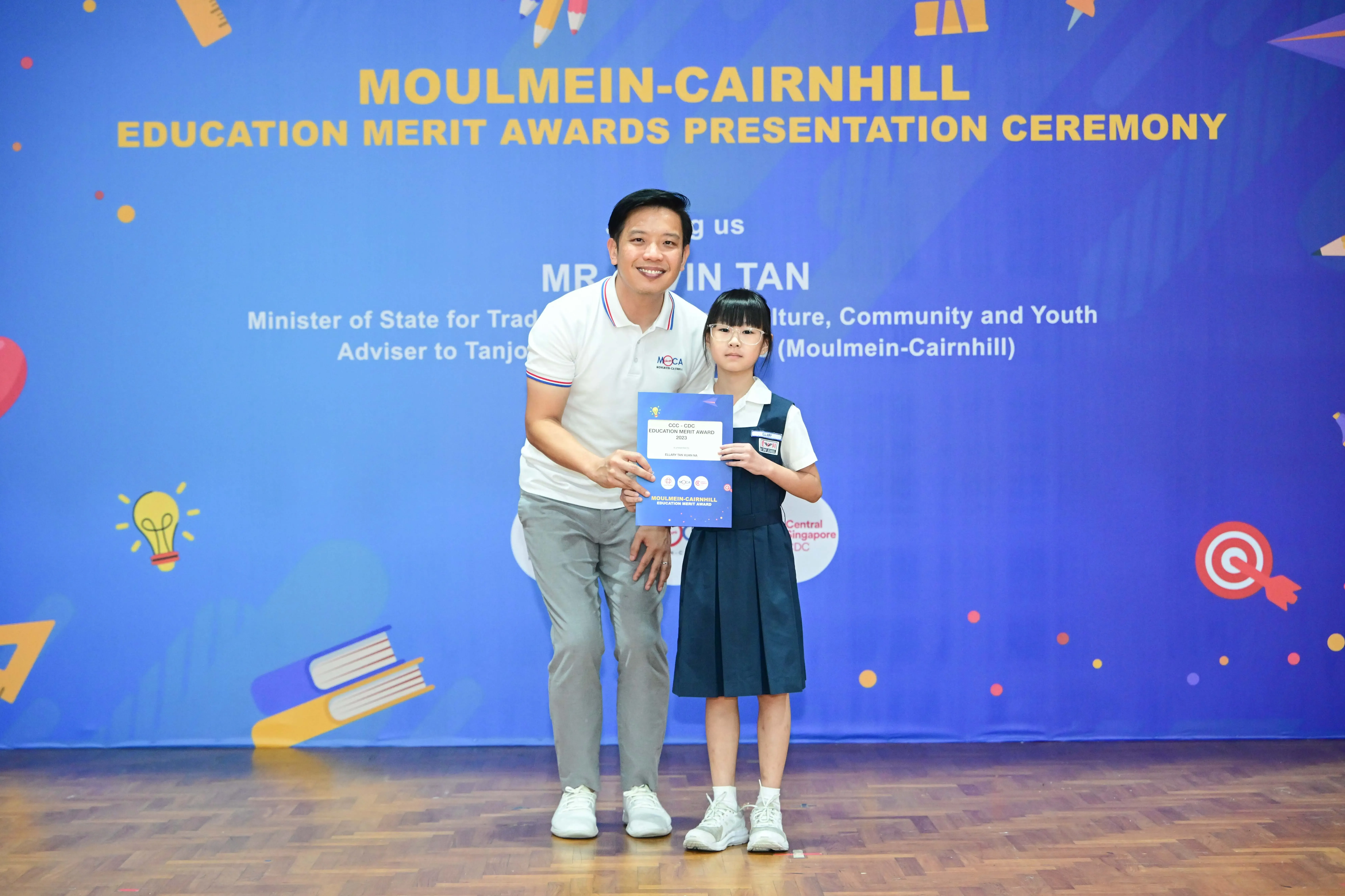 A man and a young girl in school uniform hold an award certificate at the Moulmein-Cairnhill Education Merit Awards ceremony.