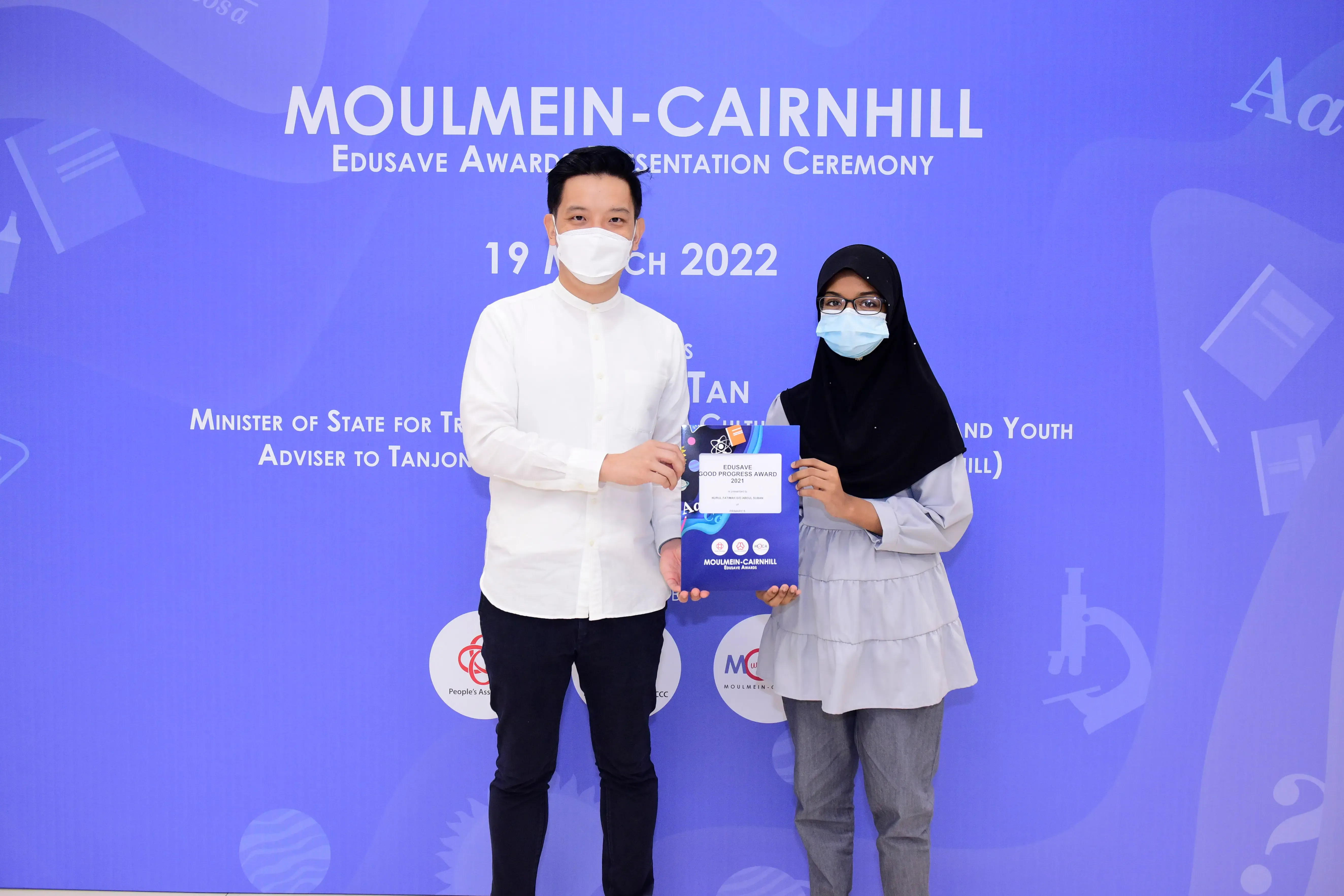 Two masked people pose holding an Edusave award at the Moulmein-Cairnhill Award Ceremony on 19 March 2022.