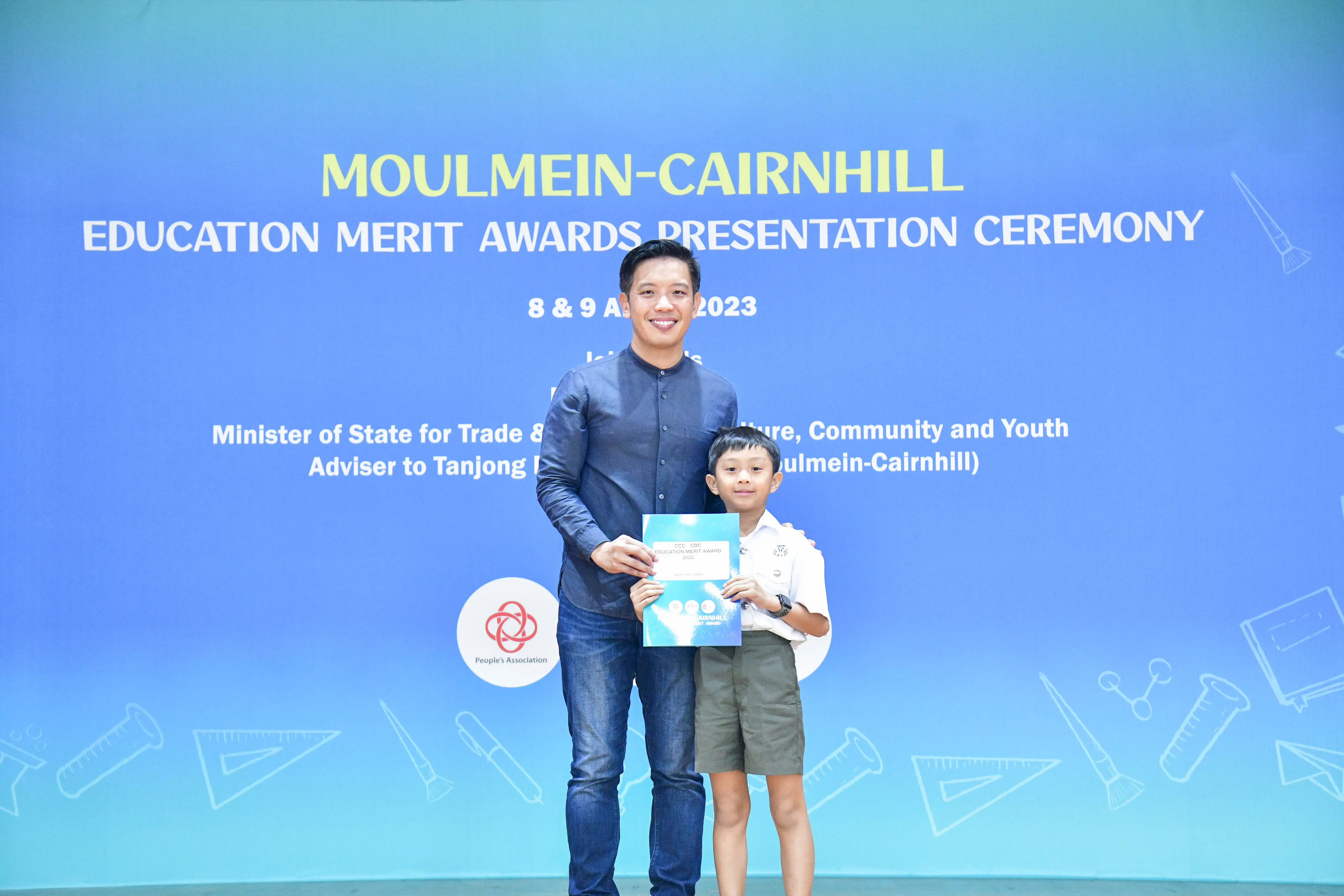 A man and a young boy hold a certificate together at the Moulmein-Cairnhill Education Merit Awards Ceremony 2023.