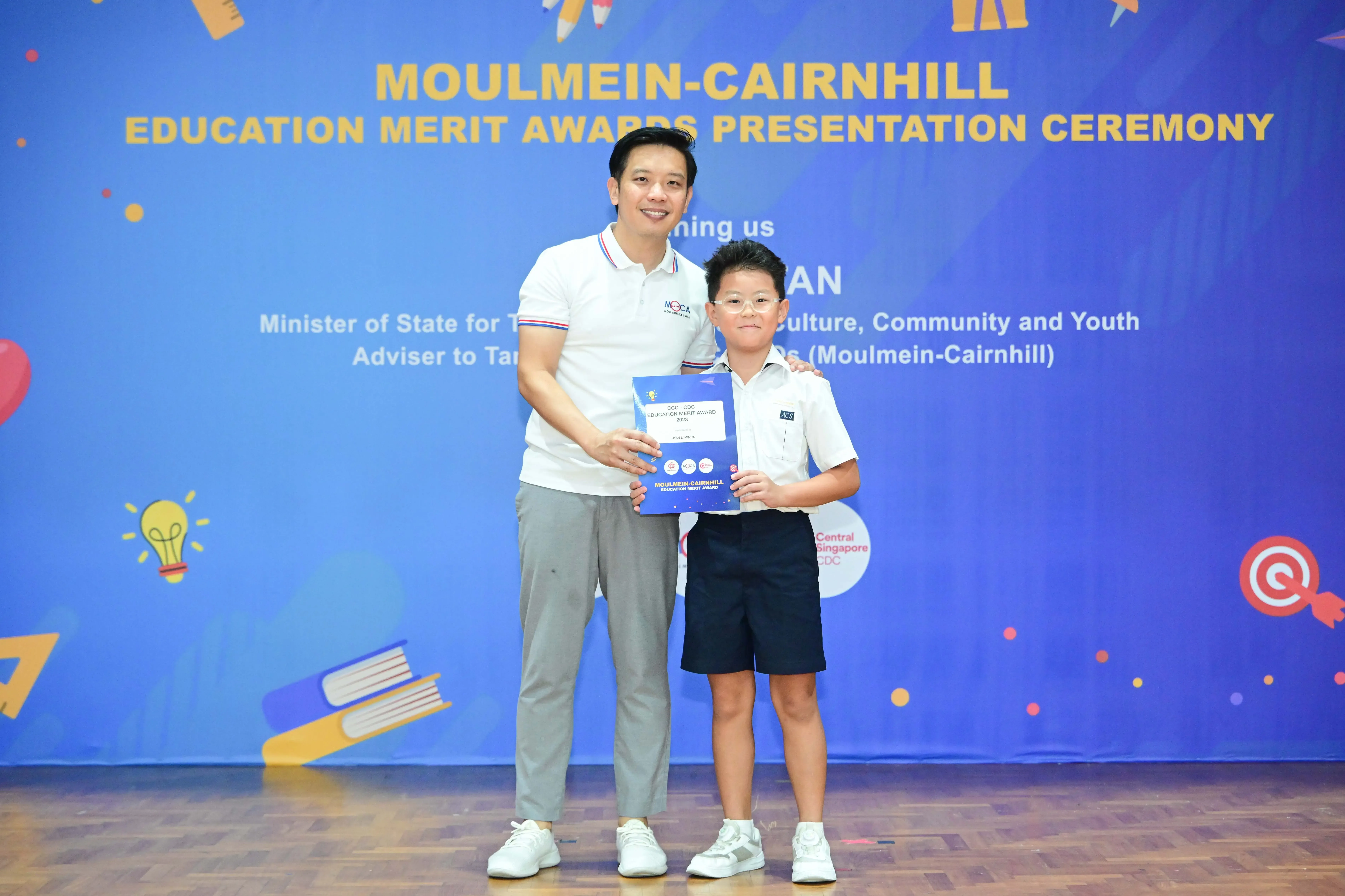 A man and a young boy pose holding an award certificate at the Moulmein-Cairnhill Education Merit Awards ceremony.