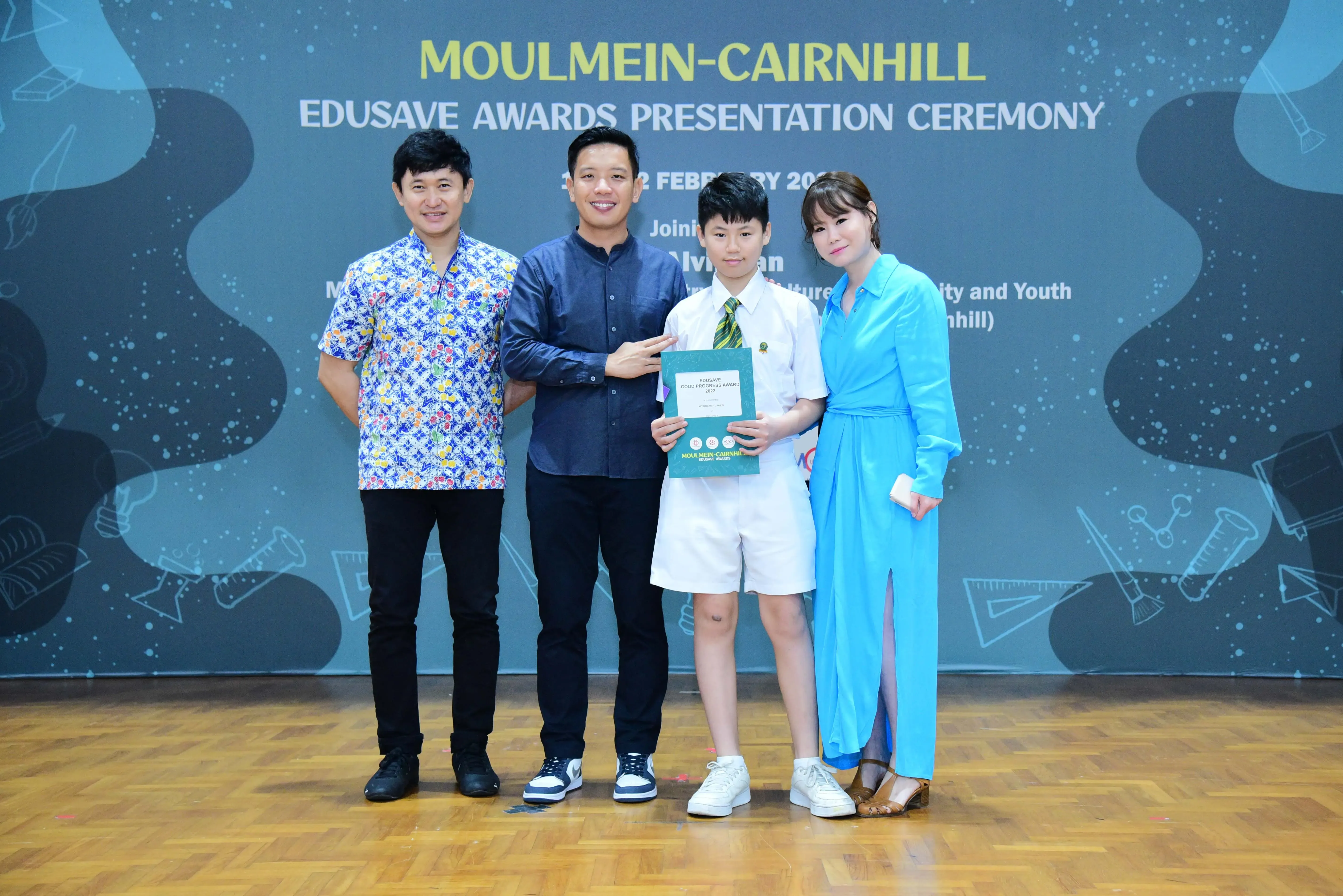 Four people pose at the Moulmein-Cairnhill Edusave Awards Presentation Ceremony, with a student holding a certificate.