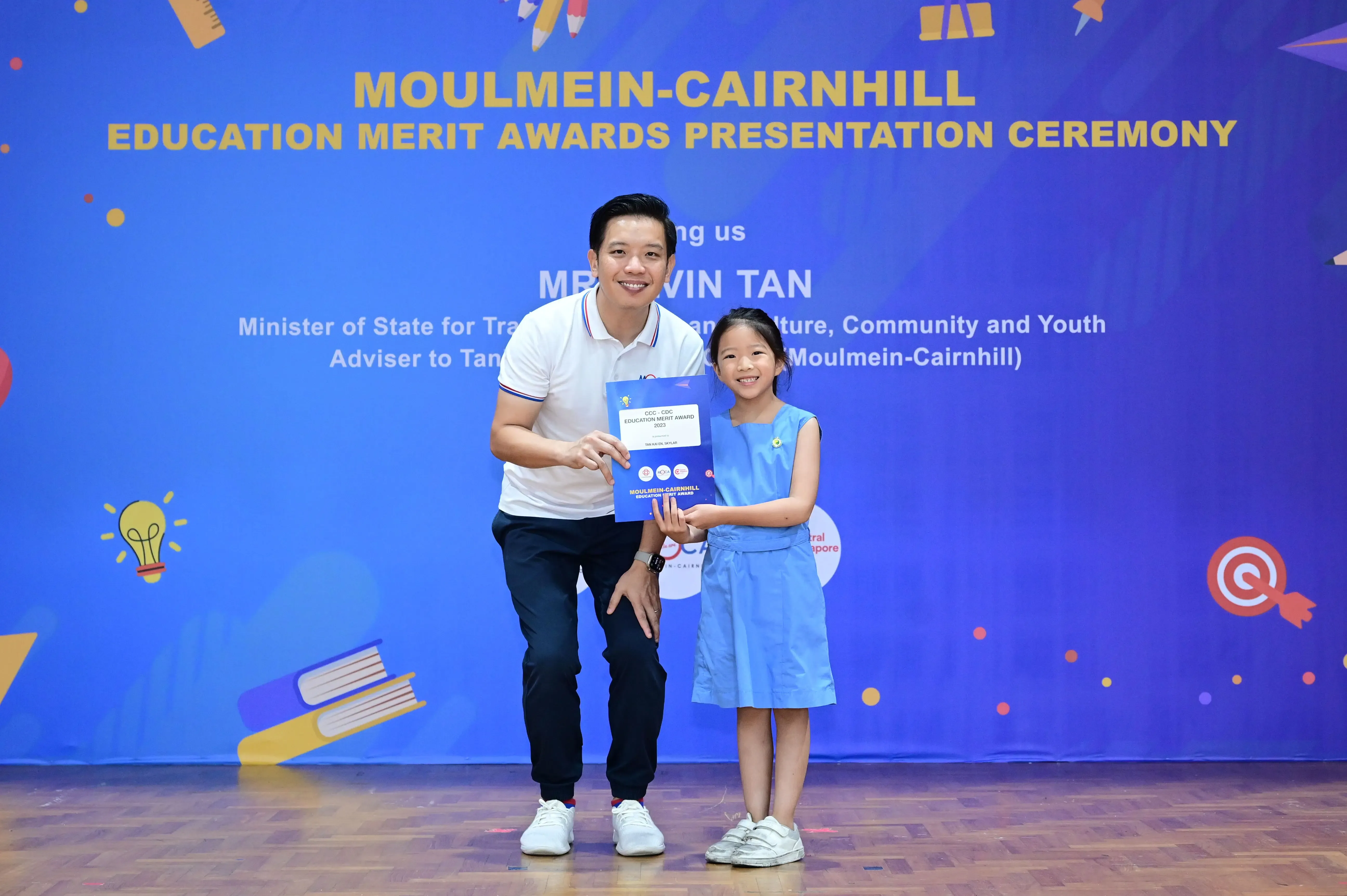 A man and a young girl hold a certificate together at the Moulmein-Cairnhill Education Merit Awards ceremony.