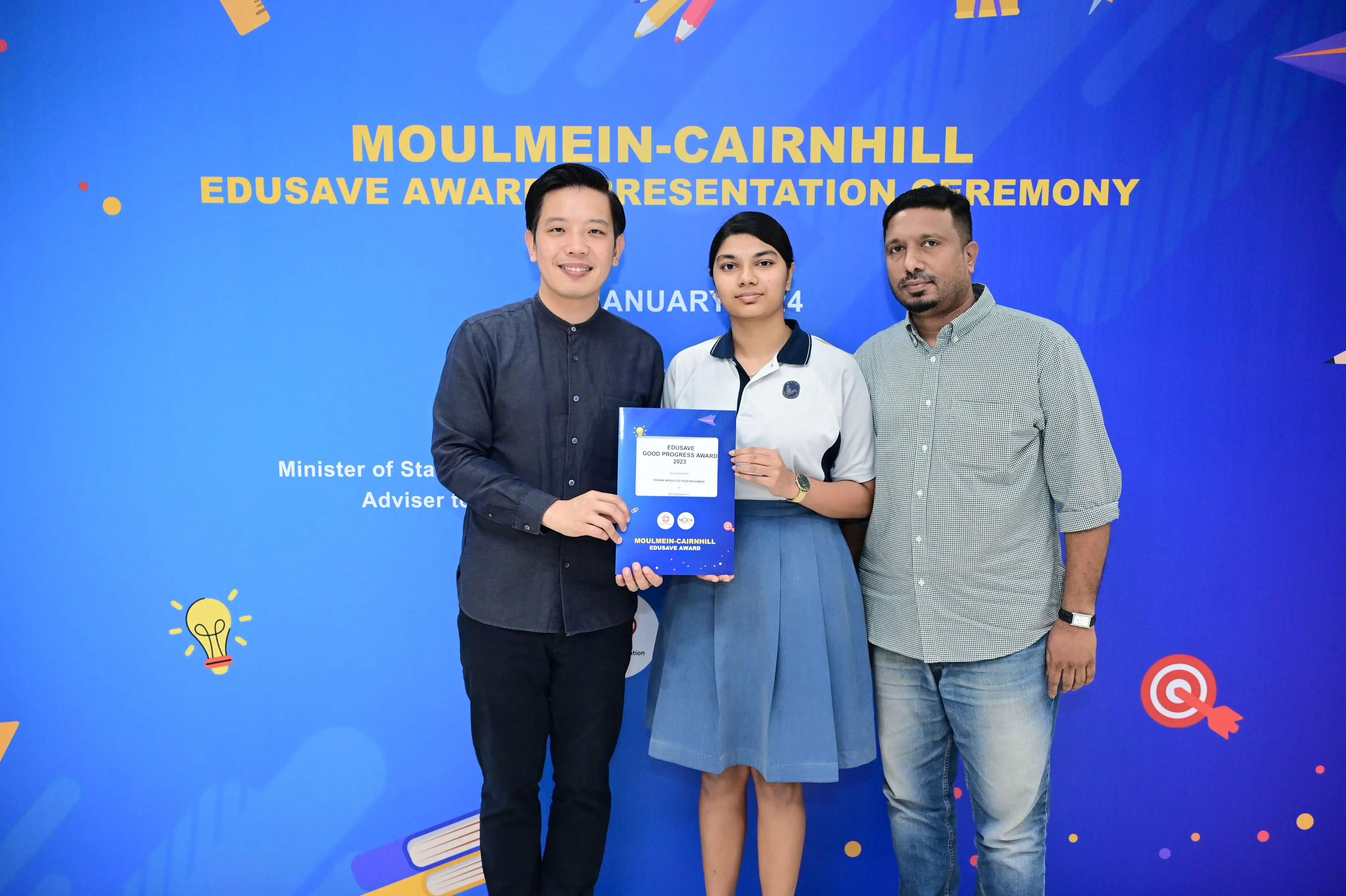 Three people pose holding an Edusave Good Progress Award certificate at the Moulmein-Cairnhill Edusave Award Ceremony.