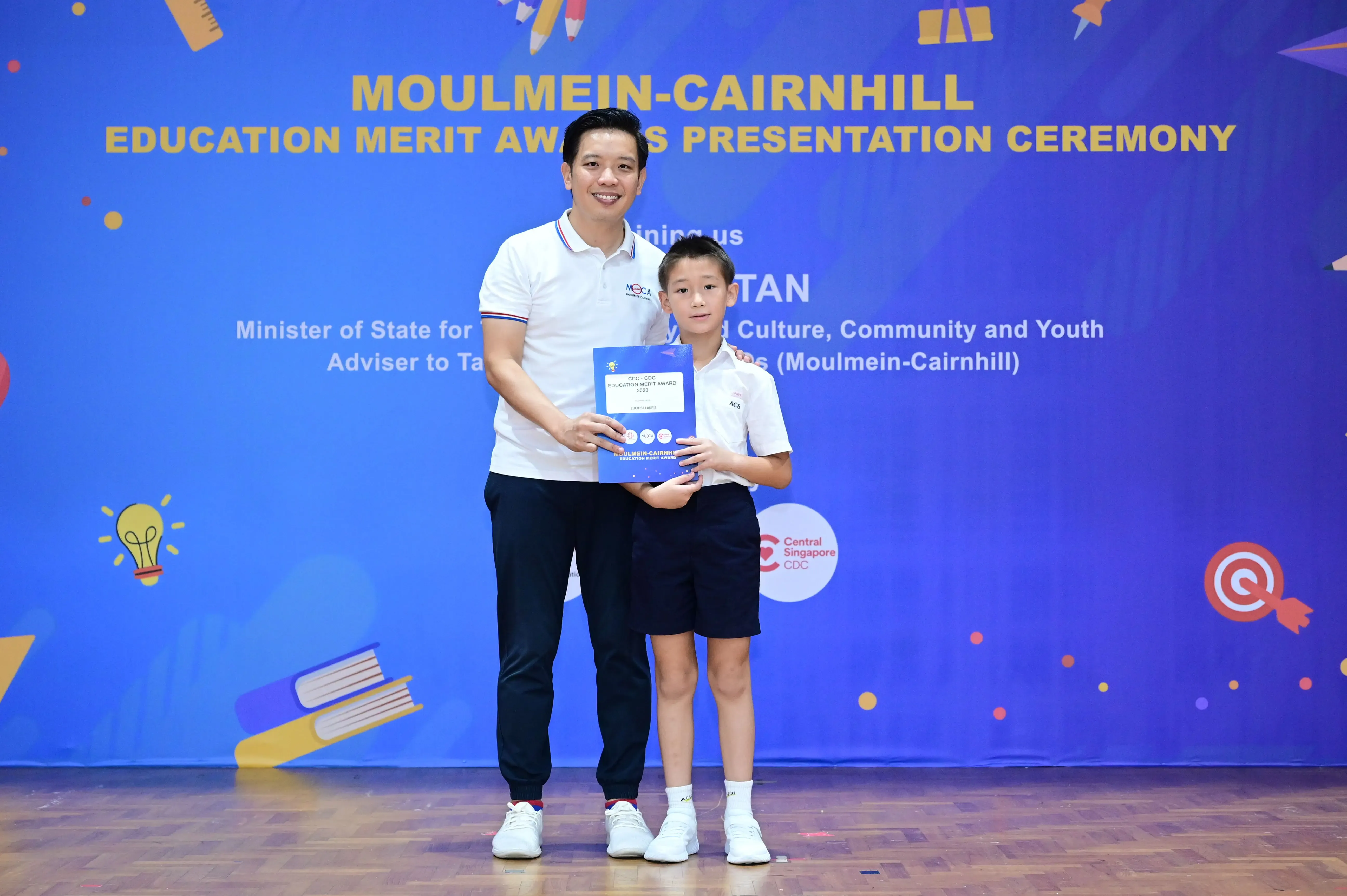 A man and a young boy hold an award certificate at the Moulmein-Cairnhill Education Merit Awards Presentation Ceremony.