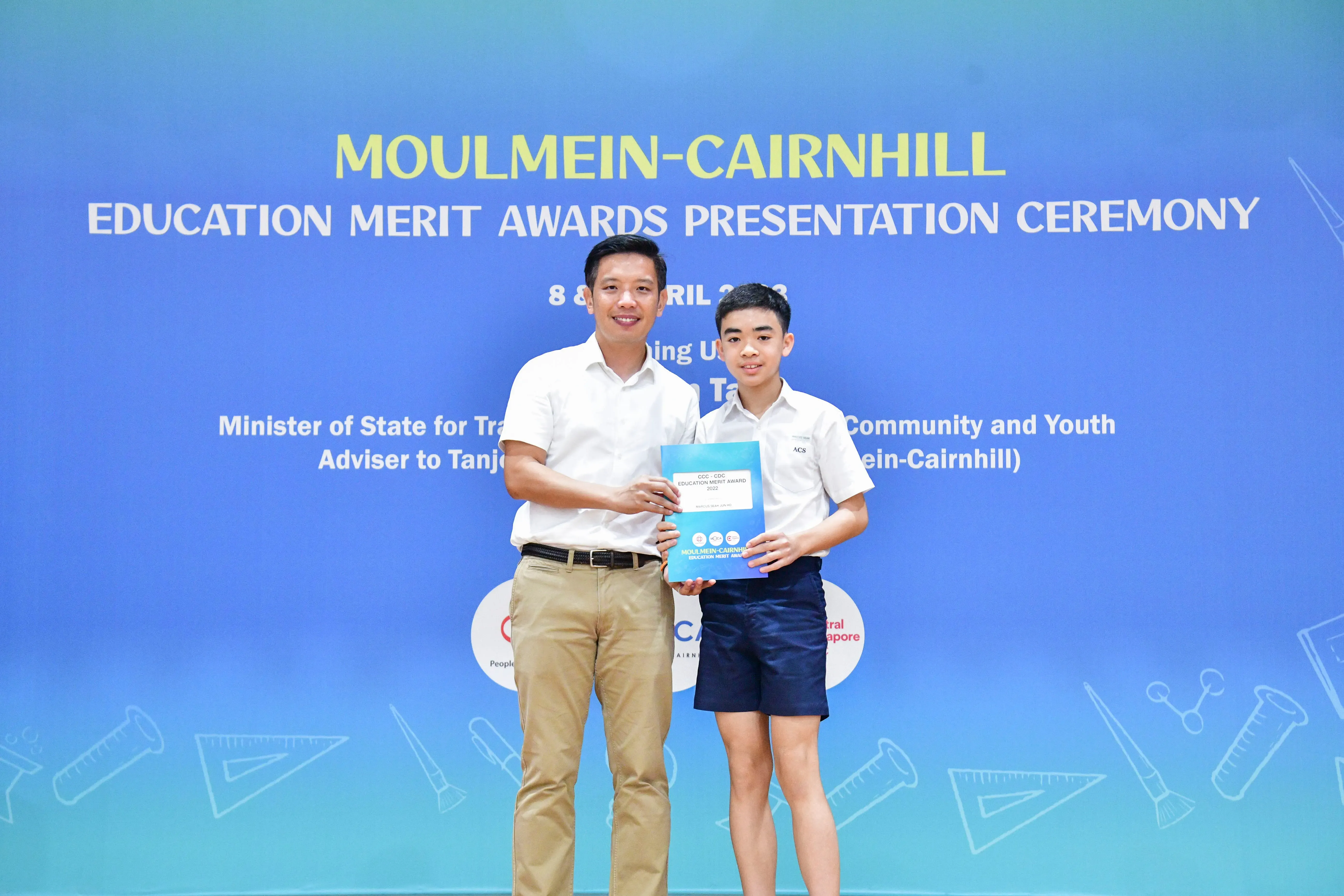 A man and a young student hold an award folder at the Moulmein-Cairnhill Education Merit Awards Ceremony.