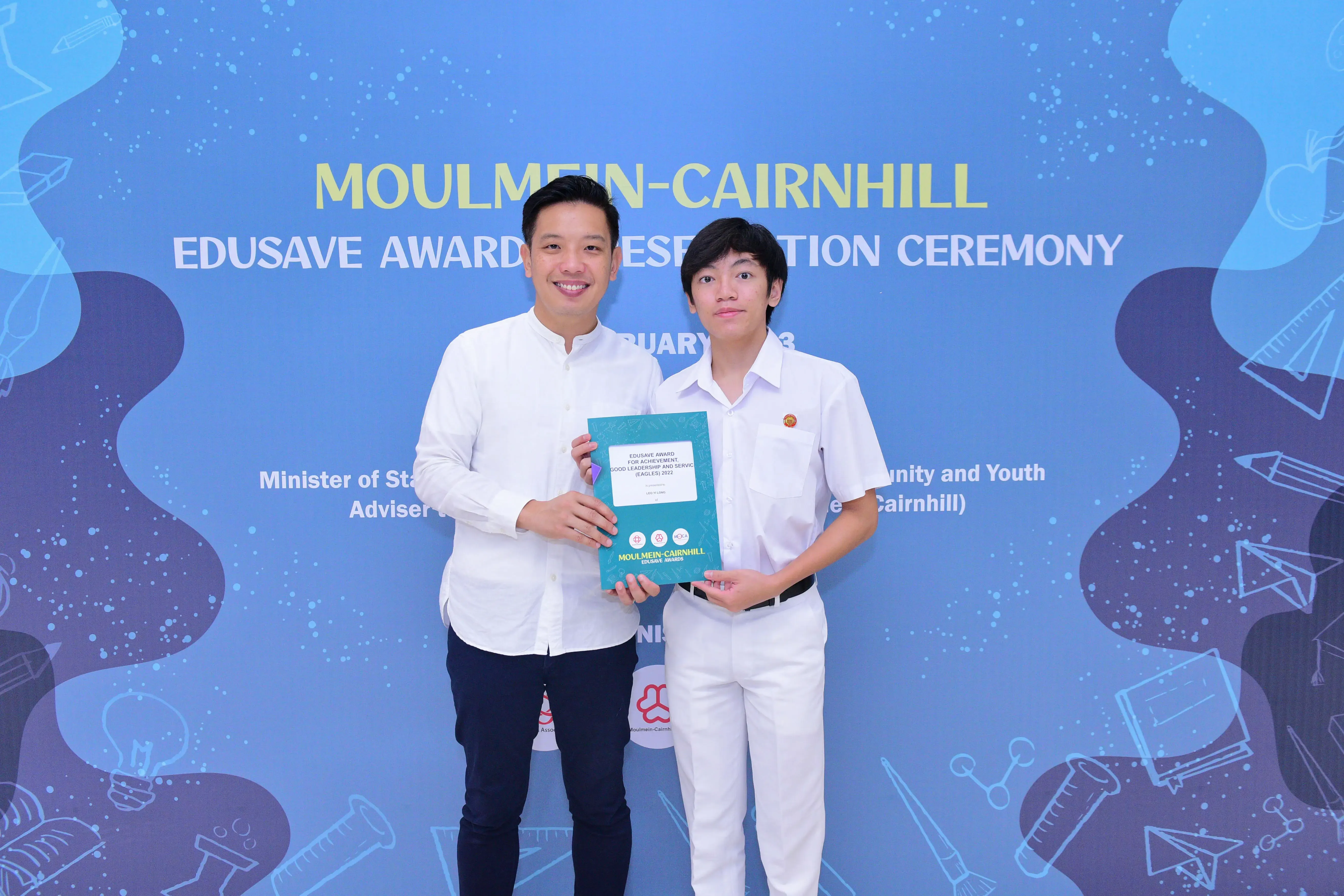 Two people hold a certificate together in front of a Moulmein-Cairnhill Edusave Awards Presentation Ceremony banner.