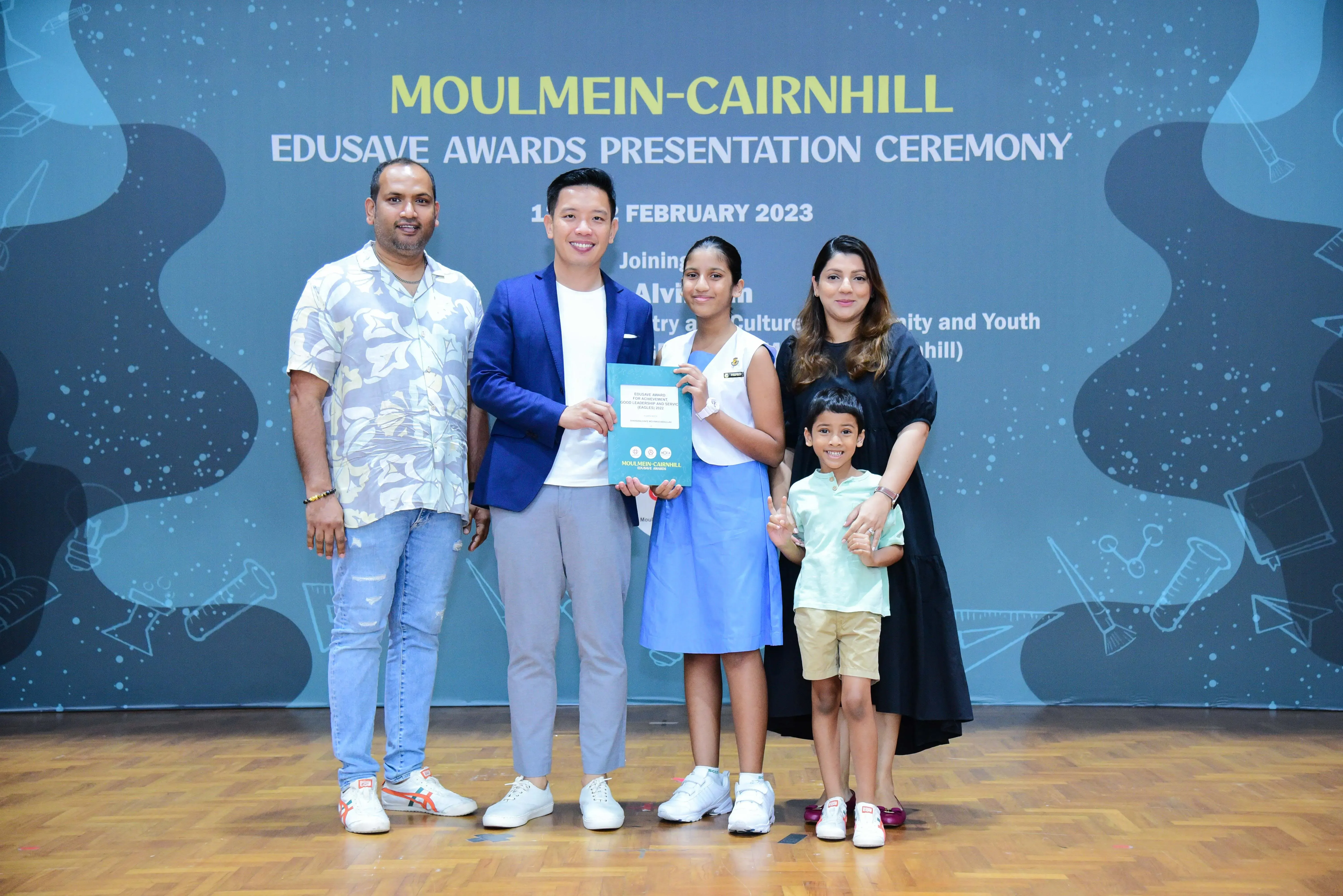 Five people pose on a stage at the Moulmein-Cairnhill Edusave Awards Presentation Ceremony, February 2023.