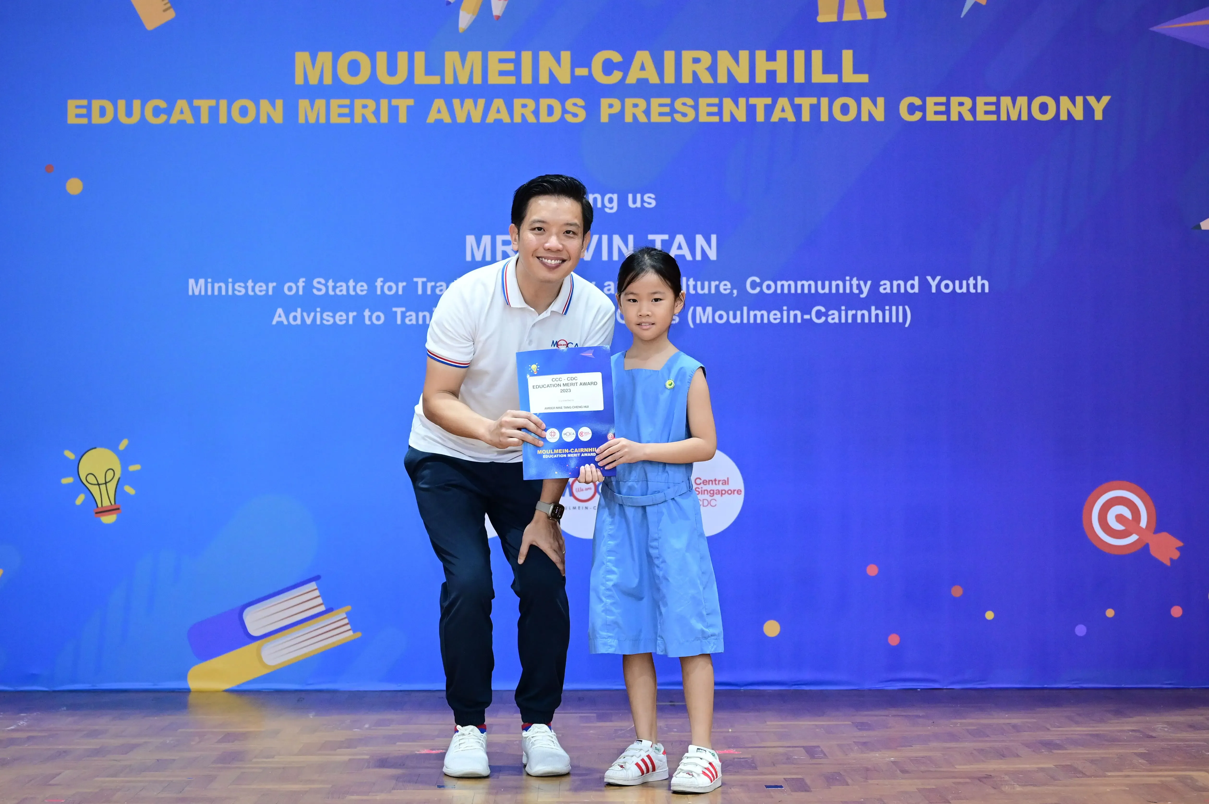 A man and a young girl hold an award certificate at the Moulmein-Cairnhill Education Merit Awards Presentation Ceremony.