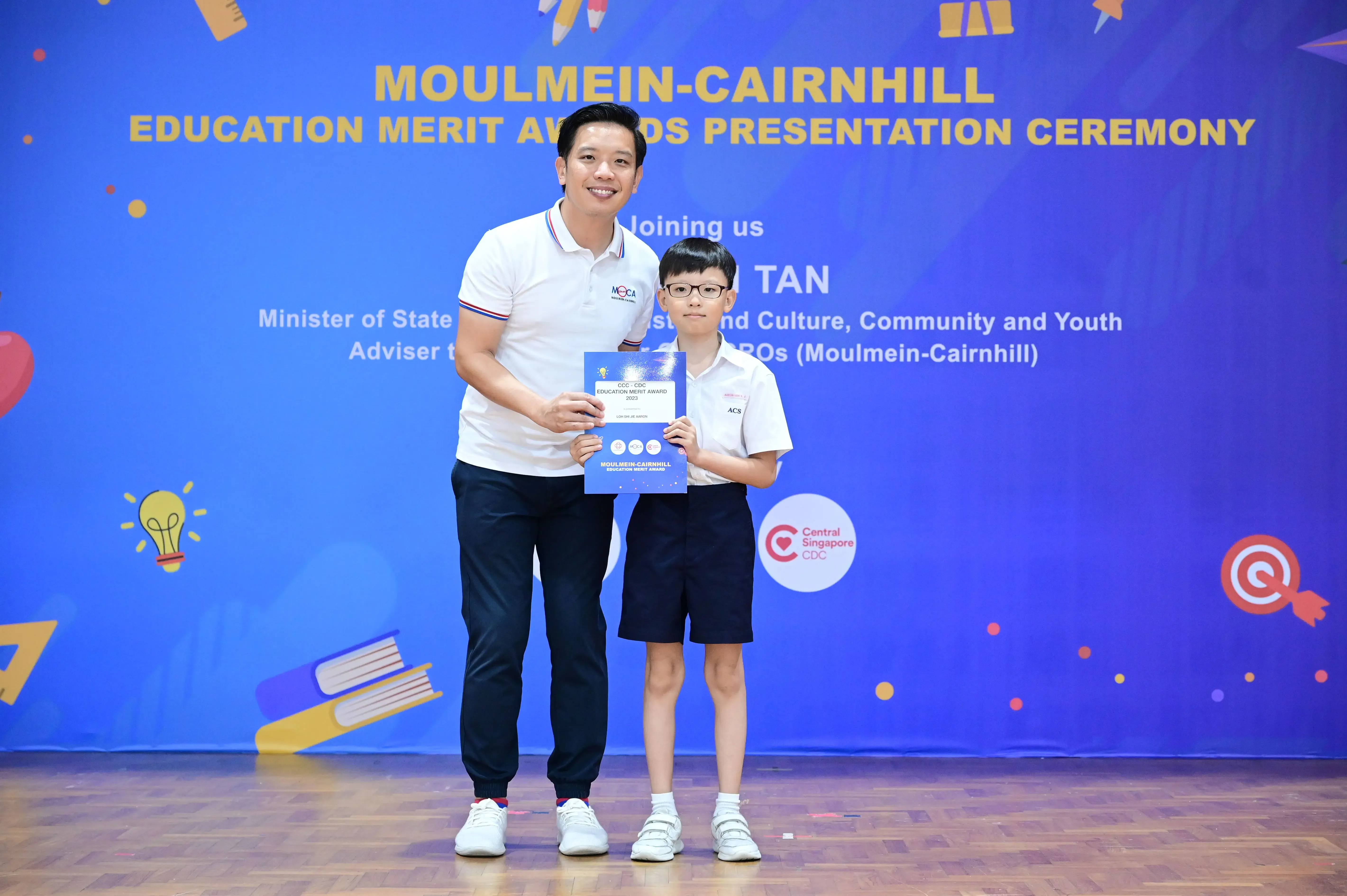 An adult and a young boy hold a certificate at the Moulmein-Cairnhill Education Merit Awards Presentation Ceremony.