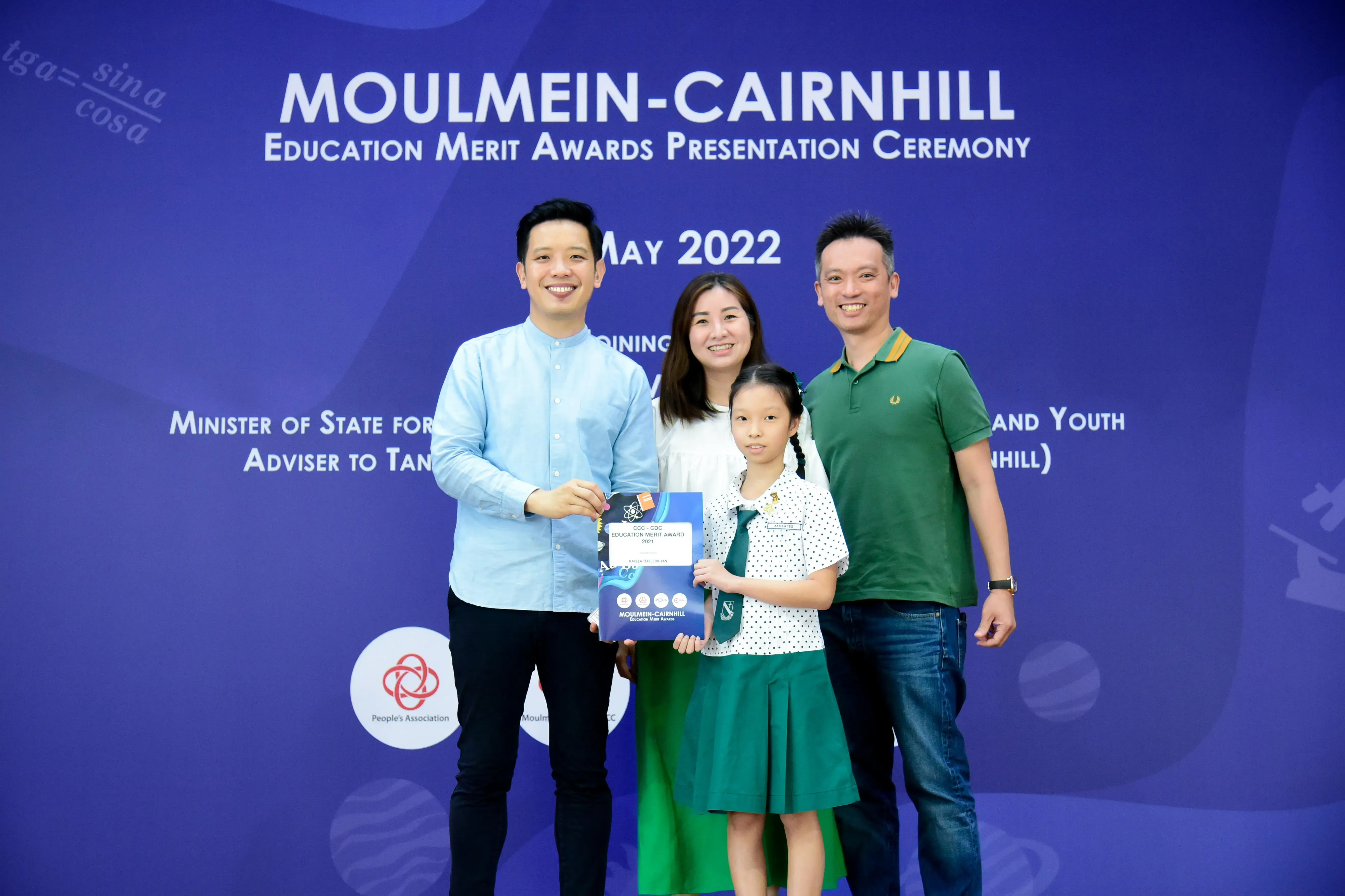 Four people pose at the Moulmein-Cairnhill Education Merit Awards Ceremony in May 2022, with a girl holding an award.