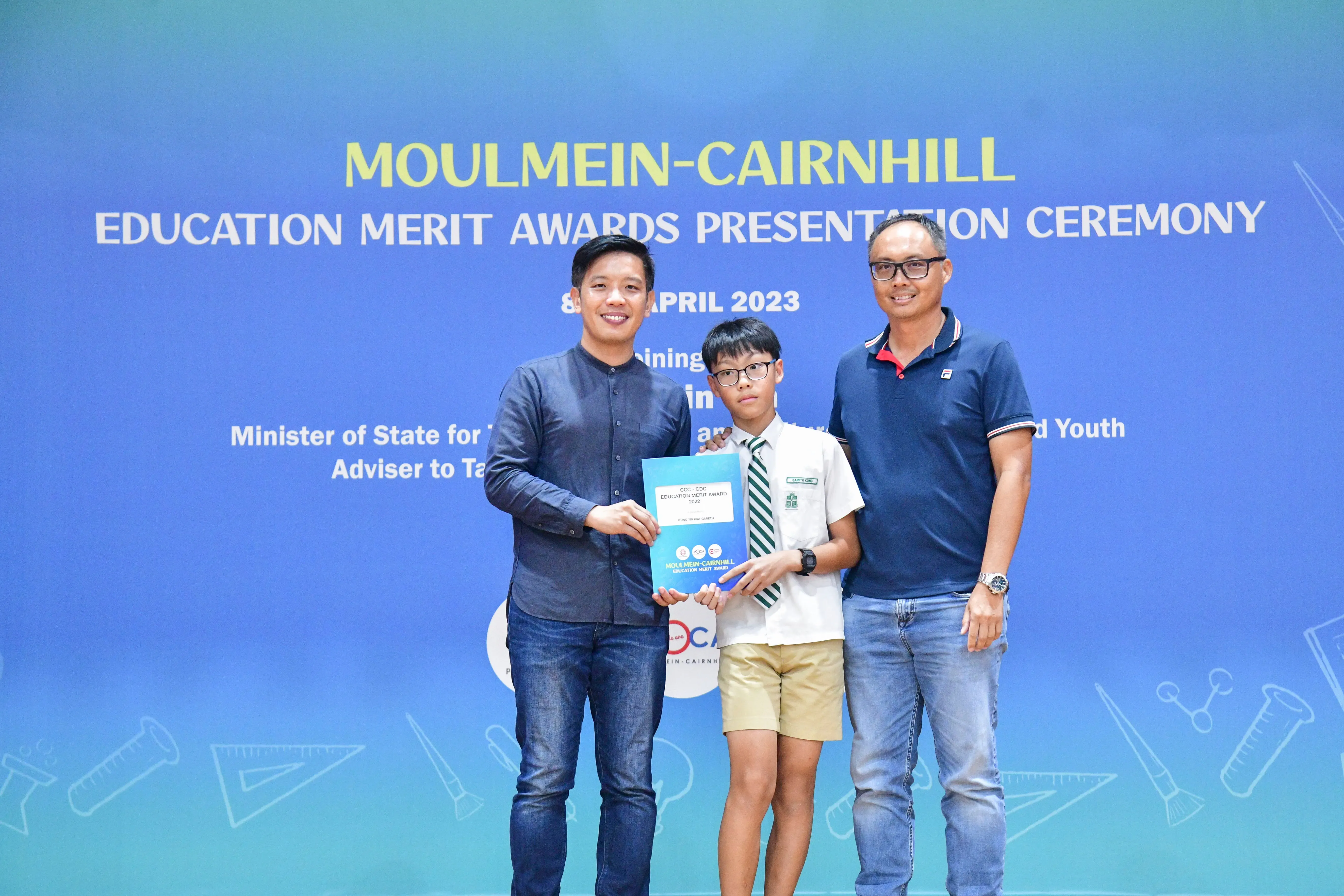 Two men and a young boy in school uniform hold an award certificate at the Moulmein-Cairnhill Education Merit Awards 2023.