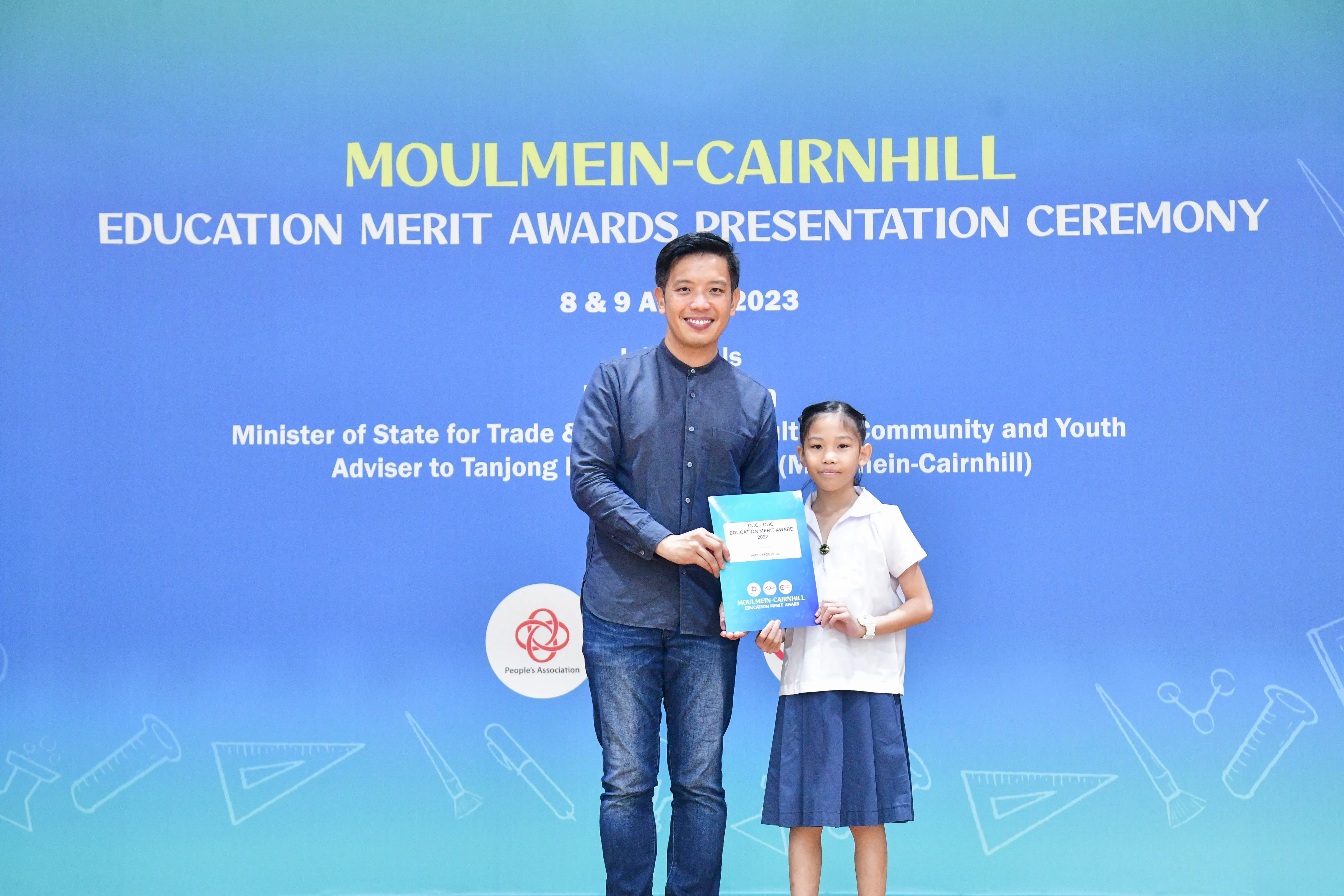 Man and young girl hold an award certificate at the Moulmein-Cairnhill Education Merit Awards Ceremony 2023.