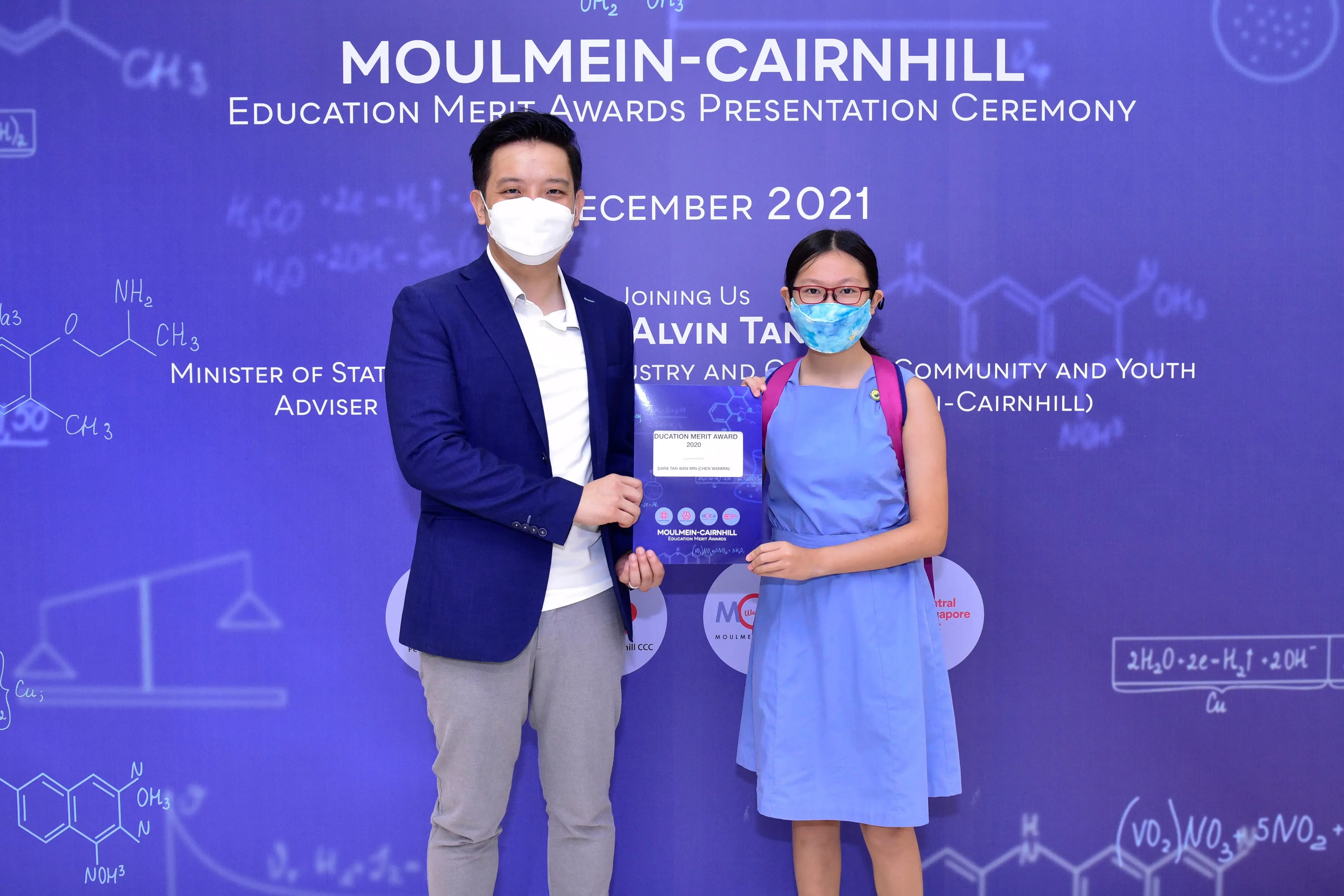 Two masked people hold an award certificate at the Moulmein-Cairnhill Education Merit Awards Ceremony, December 2021.