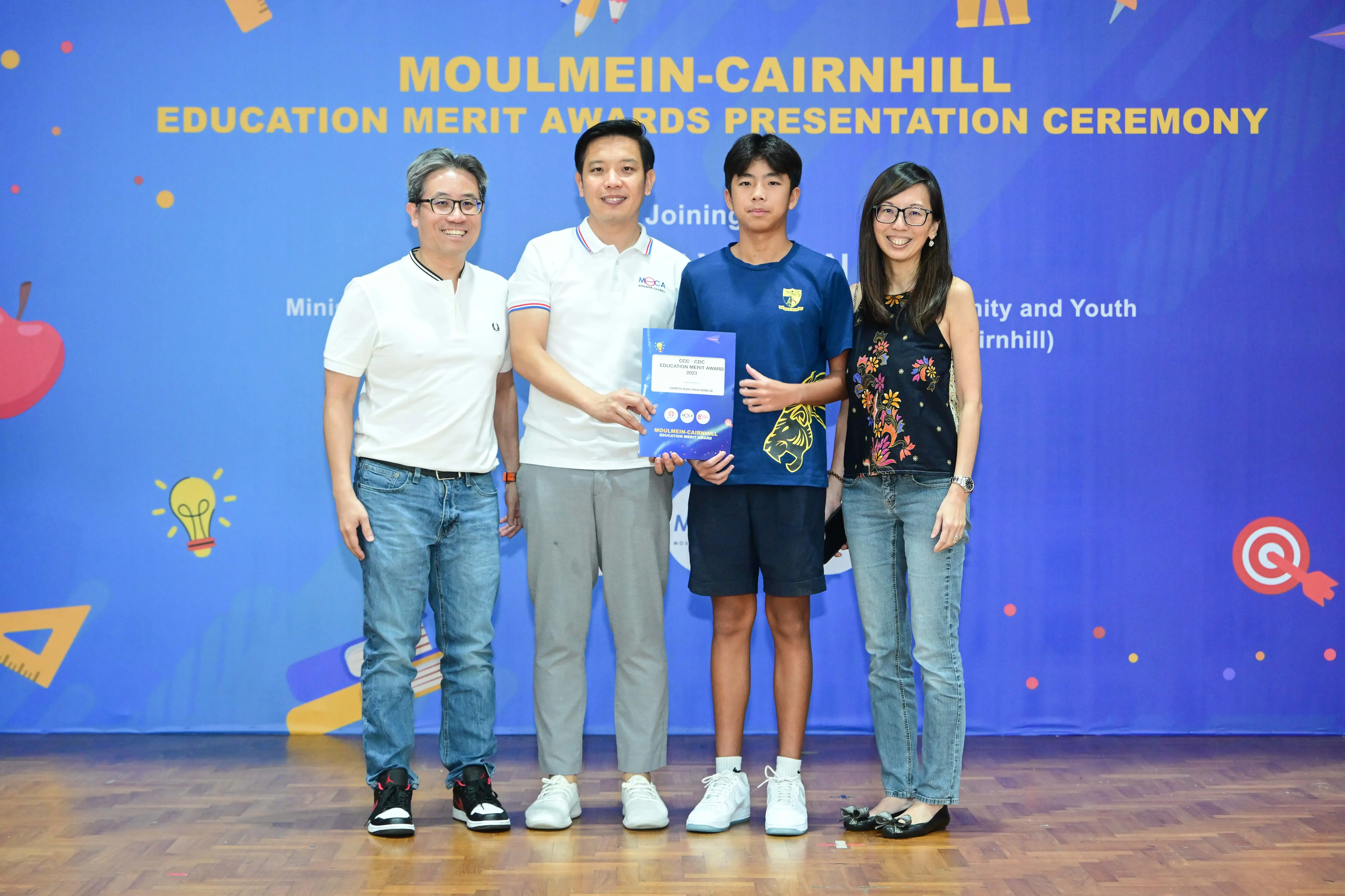 Four people pose at the Moulmein-Cairnhill Education Merit Awards Presentation Ceremony, with a teen holding an award.