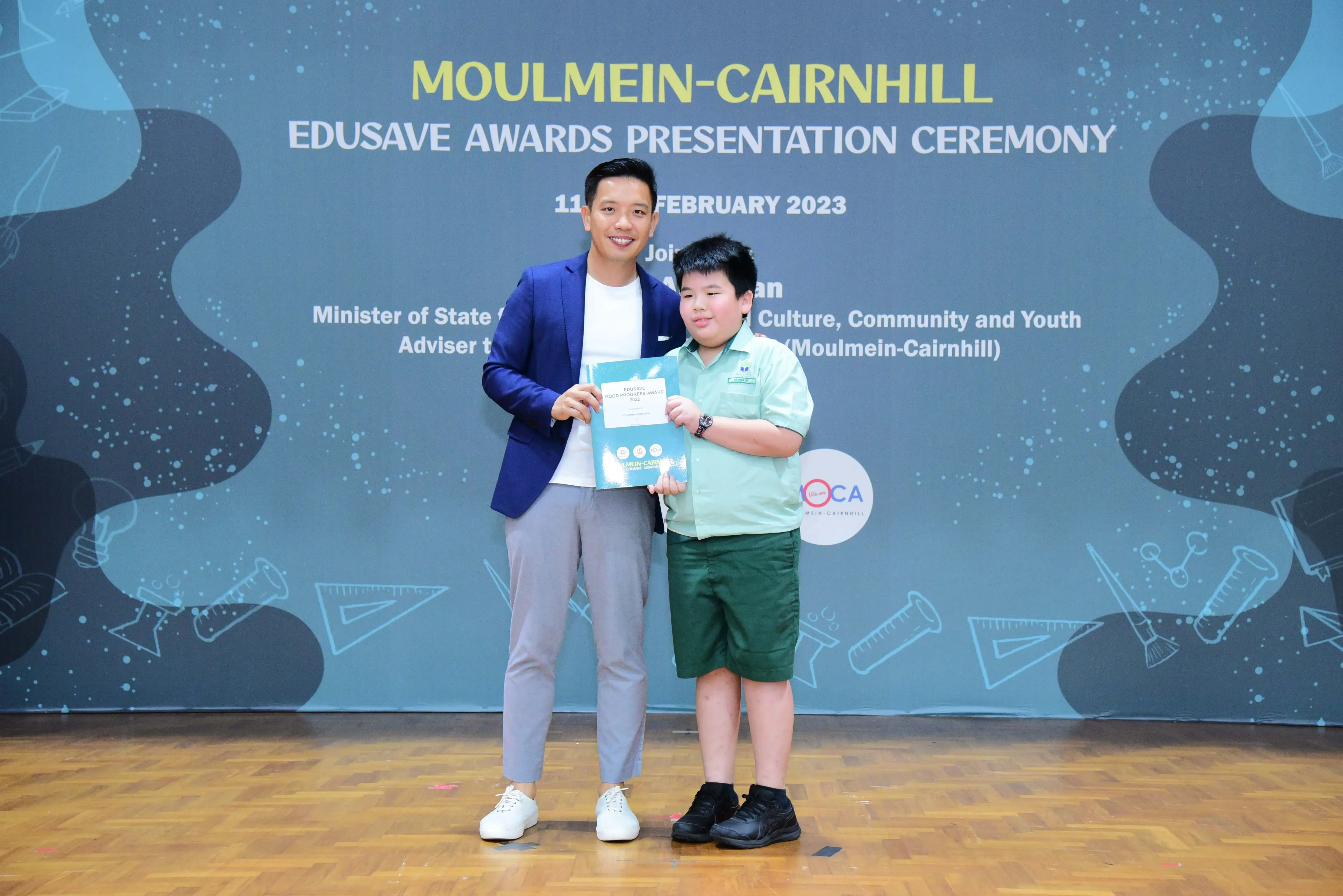 A man in a blue blazer and a young boy in school uniform pose with a certificate at the Moulmein-Cairnhill Edusave Awards 2023.