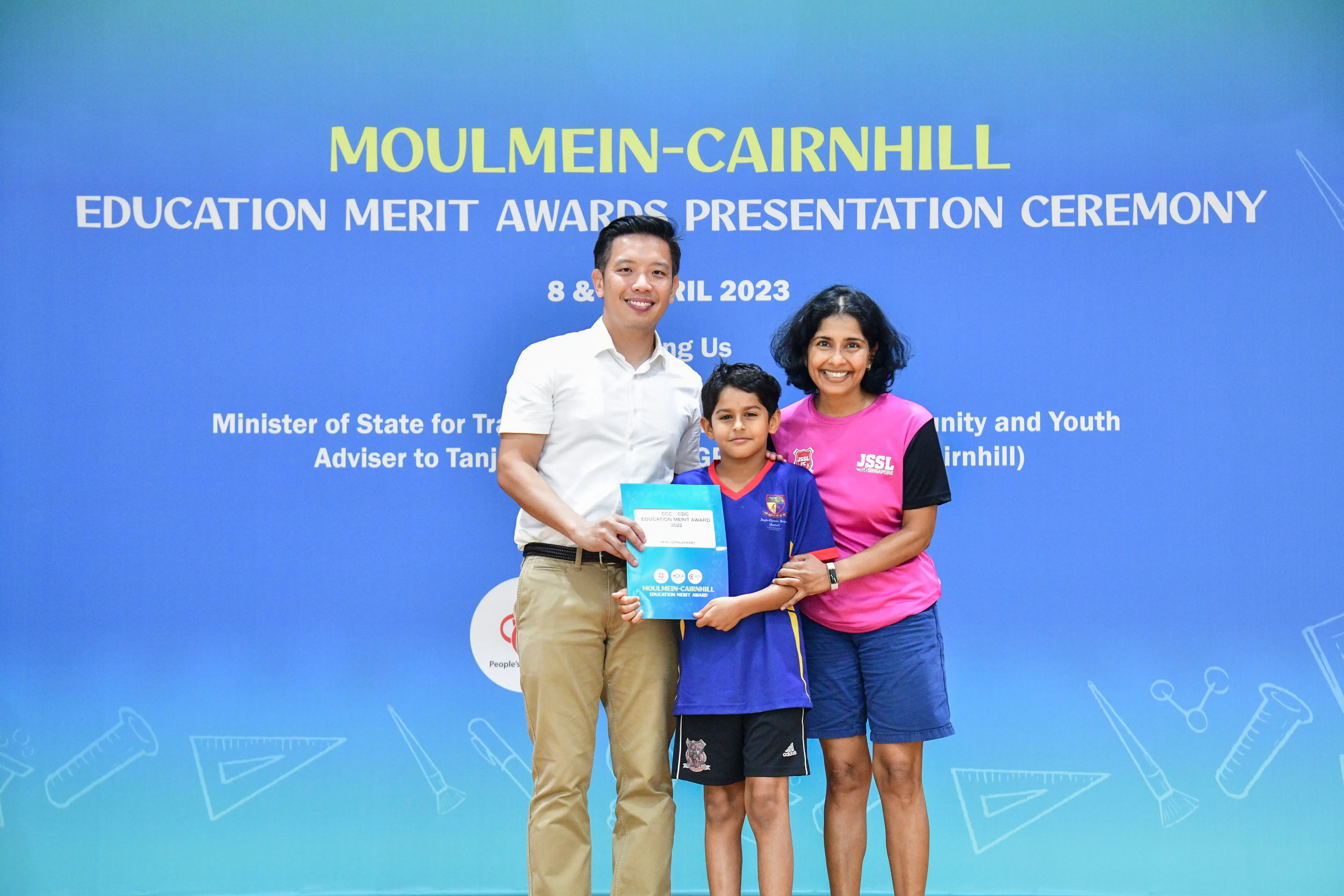 Two adults and a child pose holding an award certificate at the Moulmein-Cairnhill Education Merit Awards 2023.