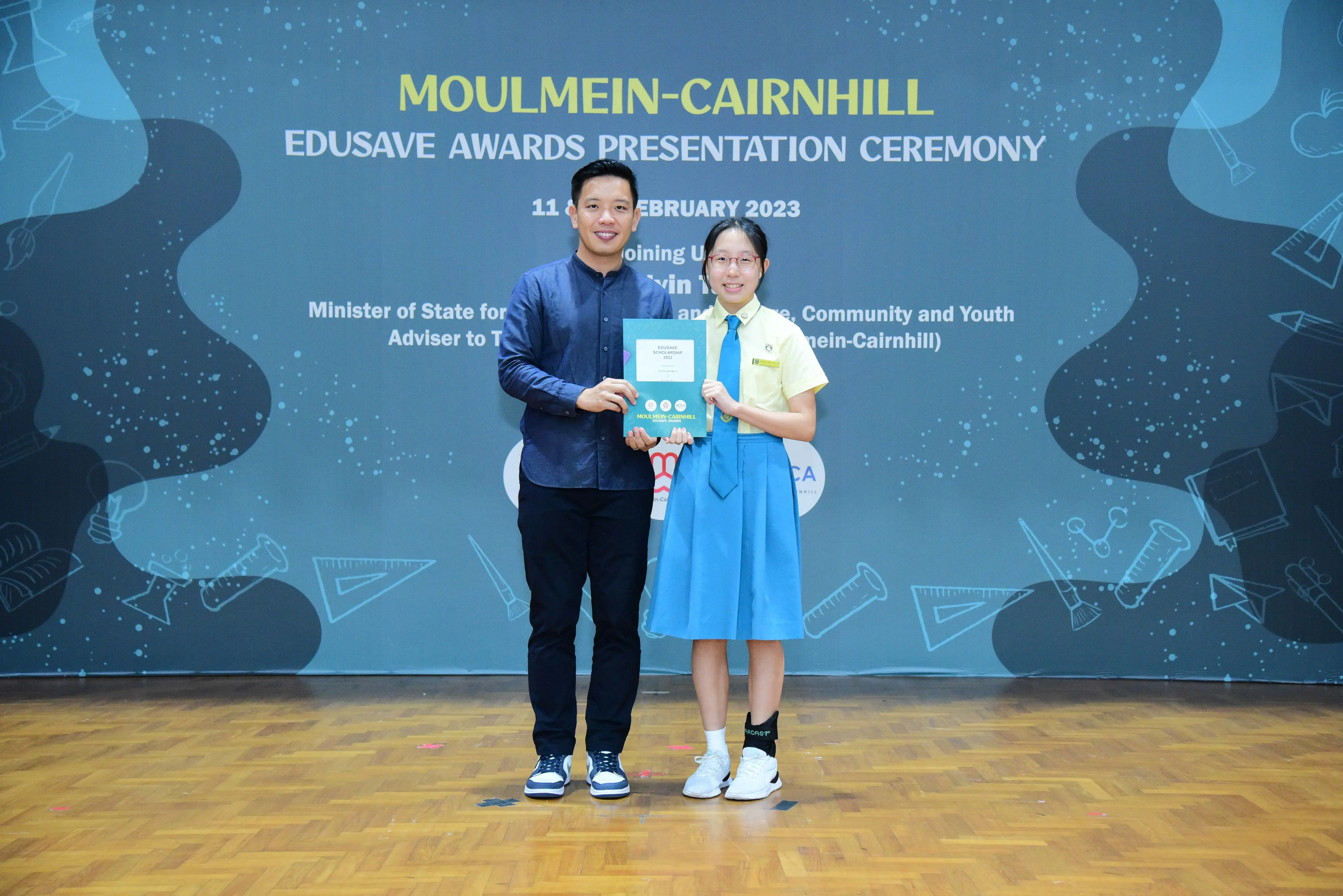 A man and a student in school uniform hold an award together at the Moulmein-Cairnhill Edusave Awards Ceremony 2023.