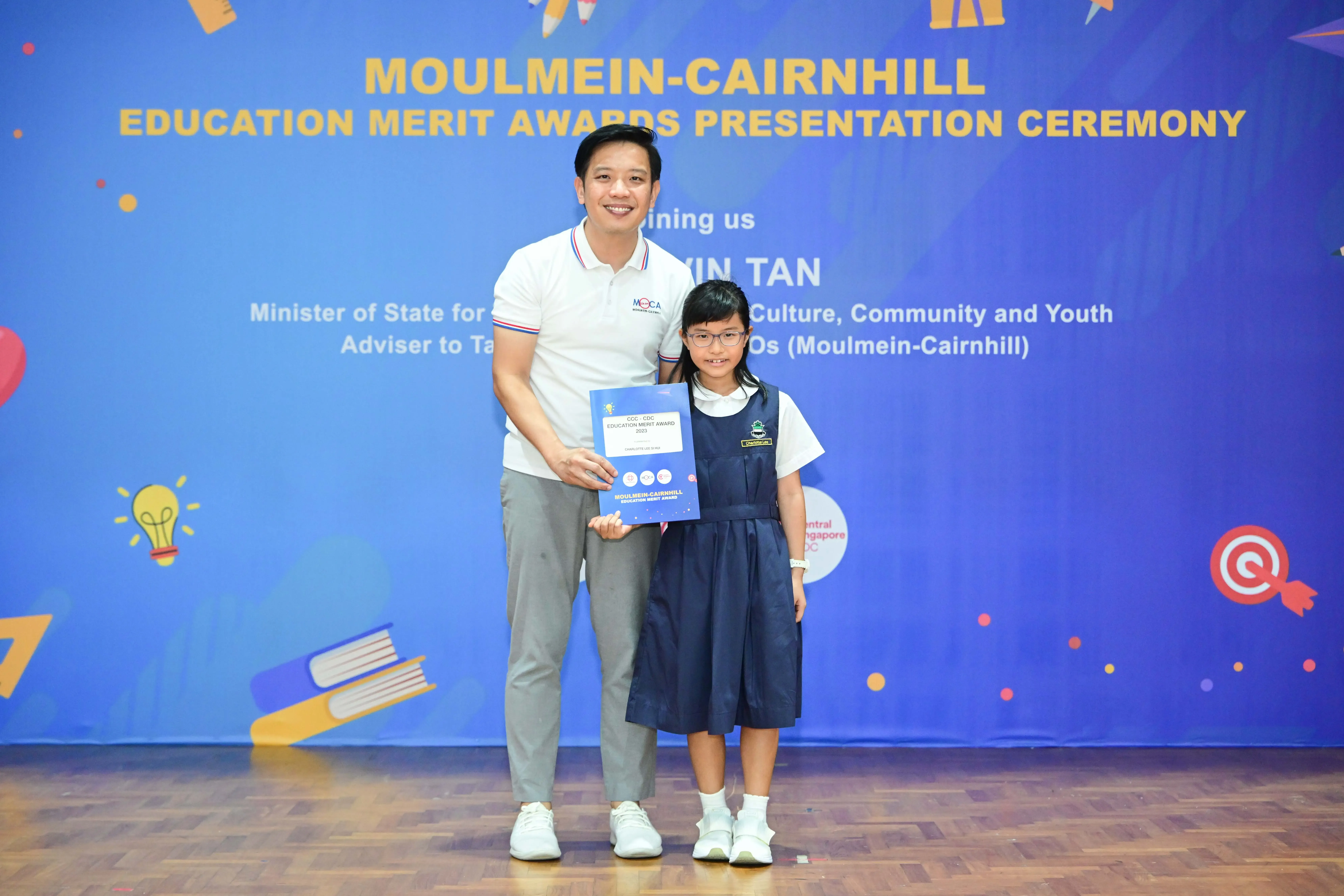 A man and a young girl in school uniform hold a certificate at the Moulmein-Cairnhill Education Merit Awards ceremony.