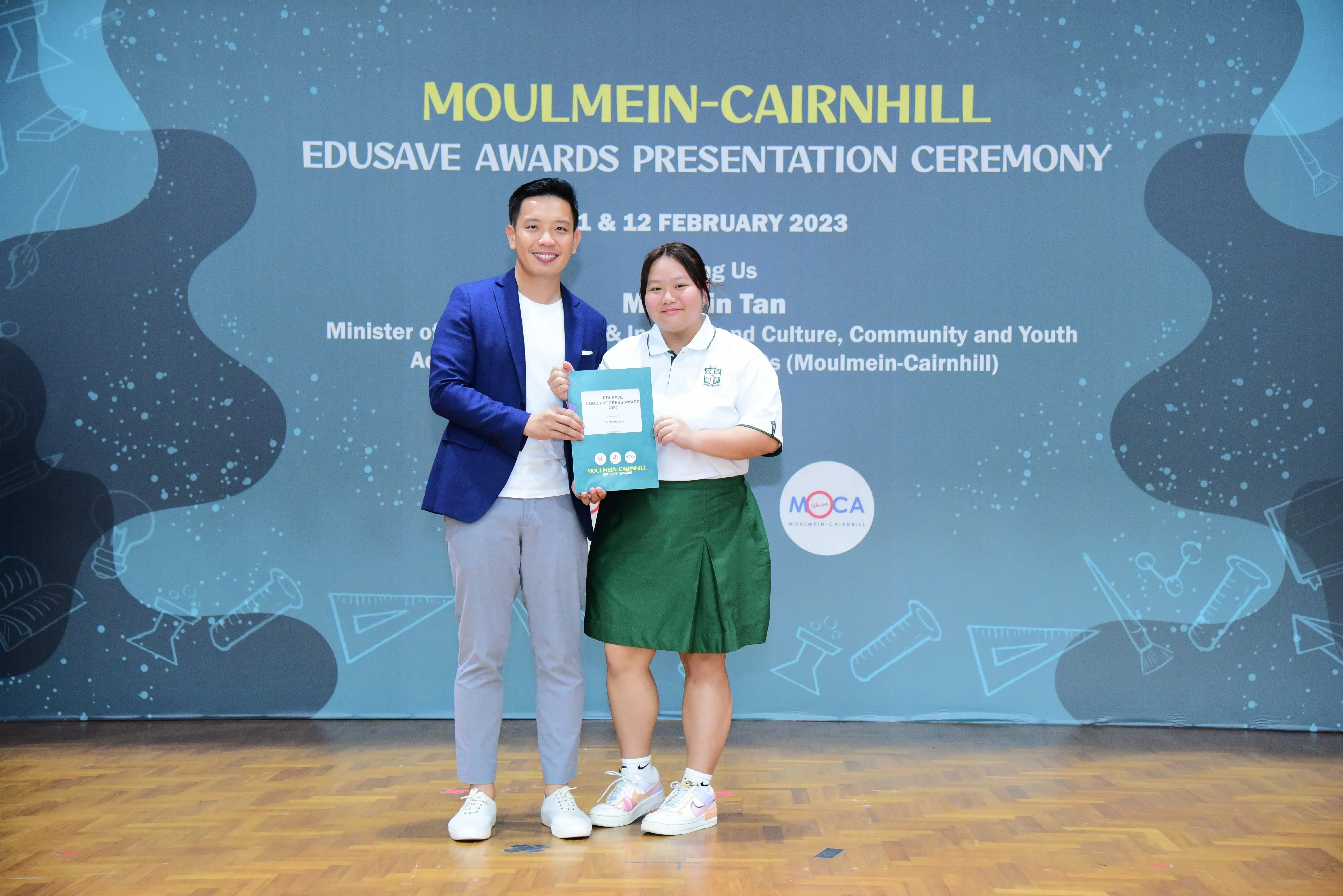 Two people hold a certificate at the Moulmein-Cairnhill Edusave Awards Presentation Ceremony, February 2023.
