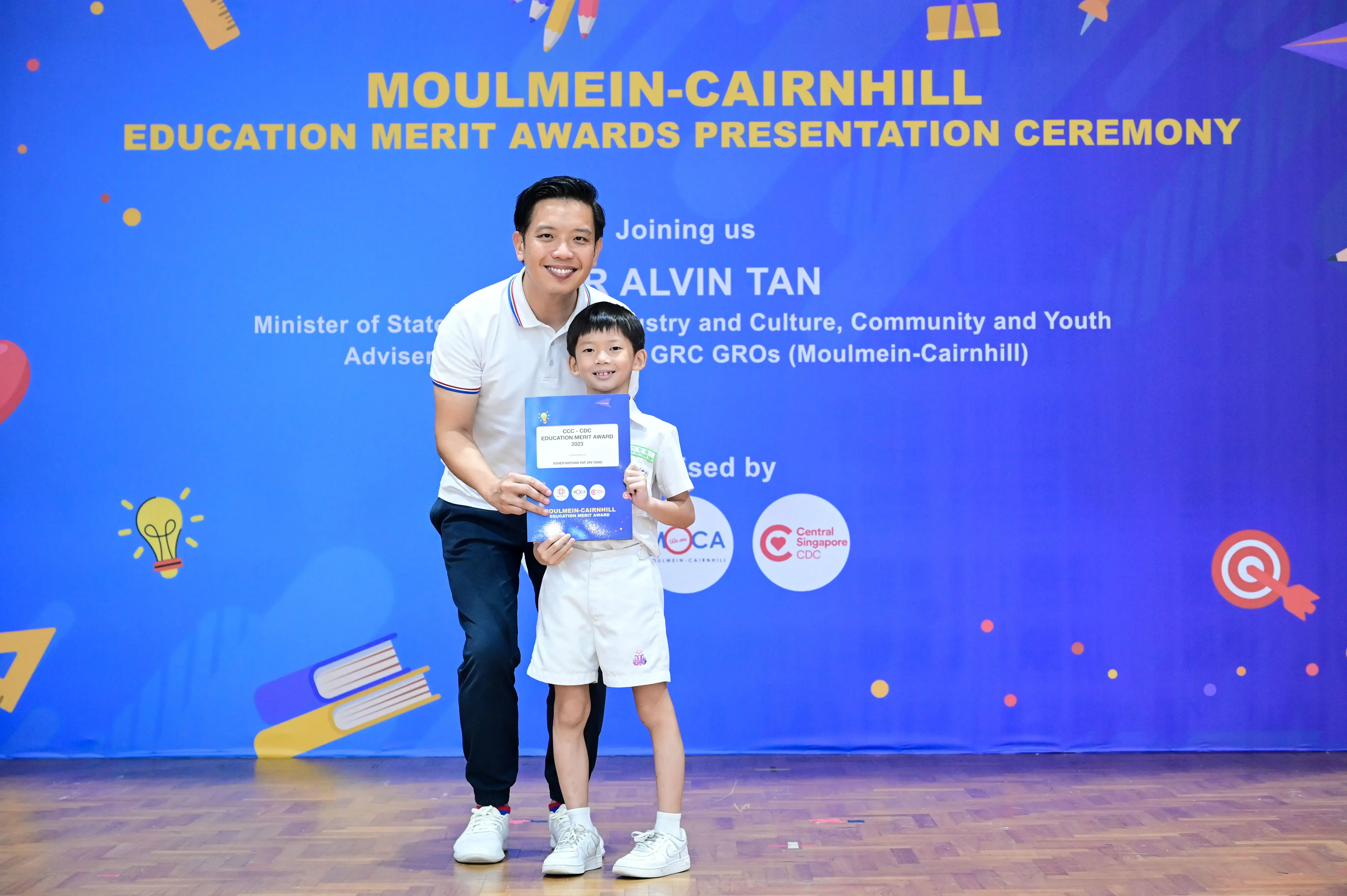 Man and young boy holding a certificate at the Moulmein-Cairnhill Education Merit Awards Presentation Ceremony.