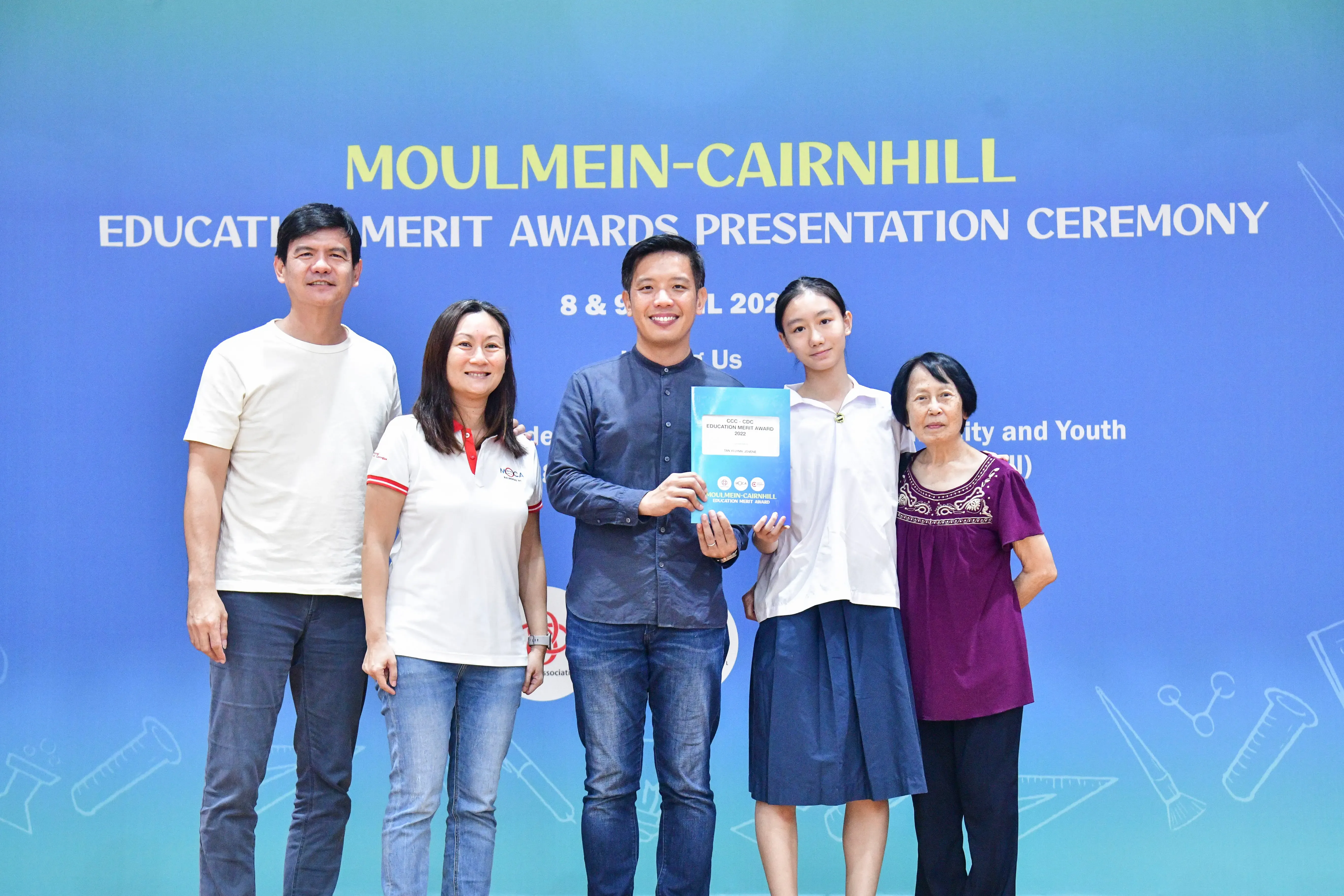 Five people pose together holding an award certificate at the Moulmein-Cairnhill Education Merit Awards Presentation Ceremony.