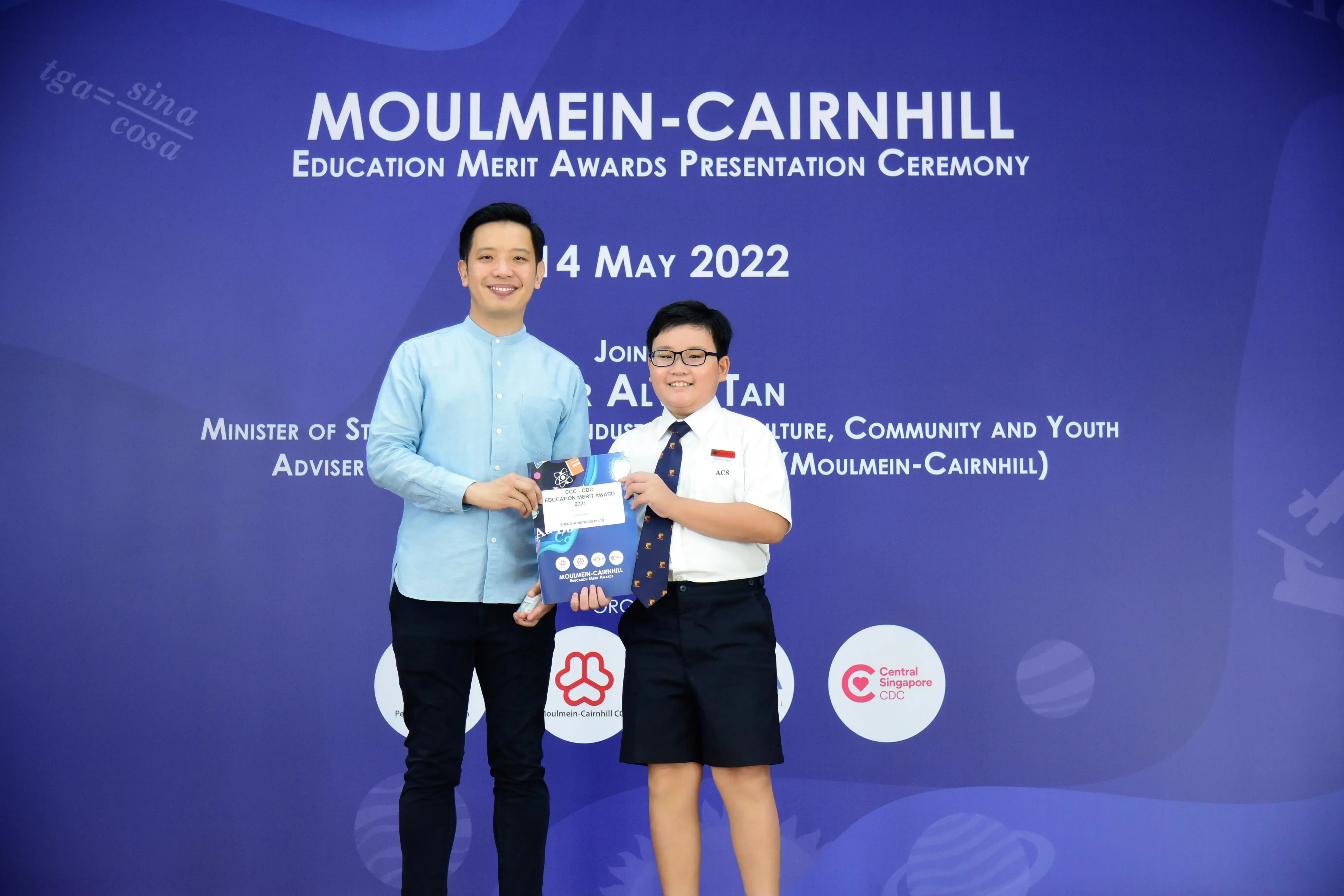 An adult and a young student in school uniform hold an award folder at the Moulmein-Cairnhill Education Merit Awards 2022.